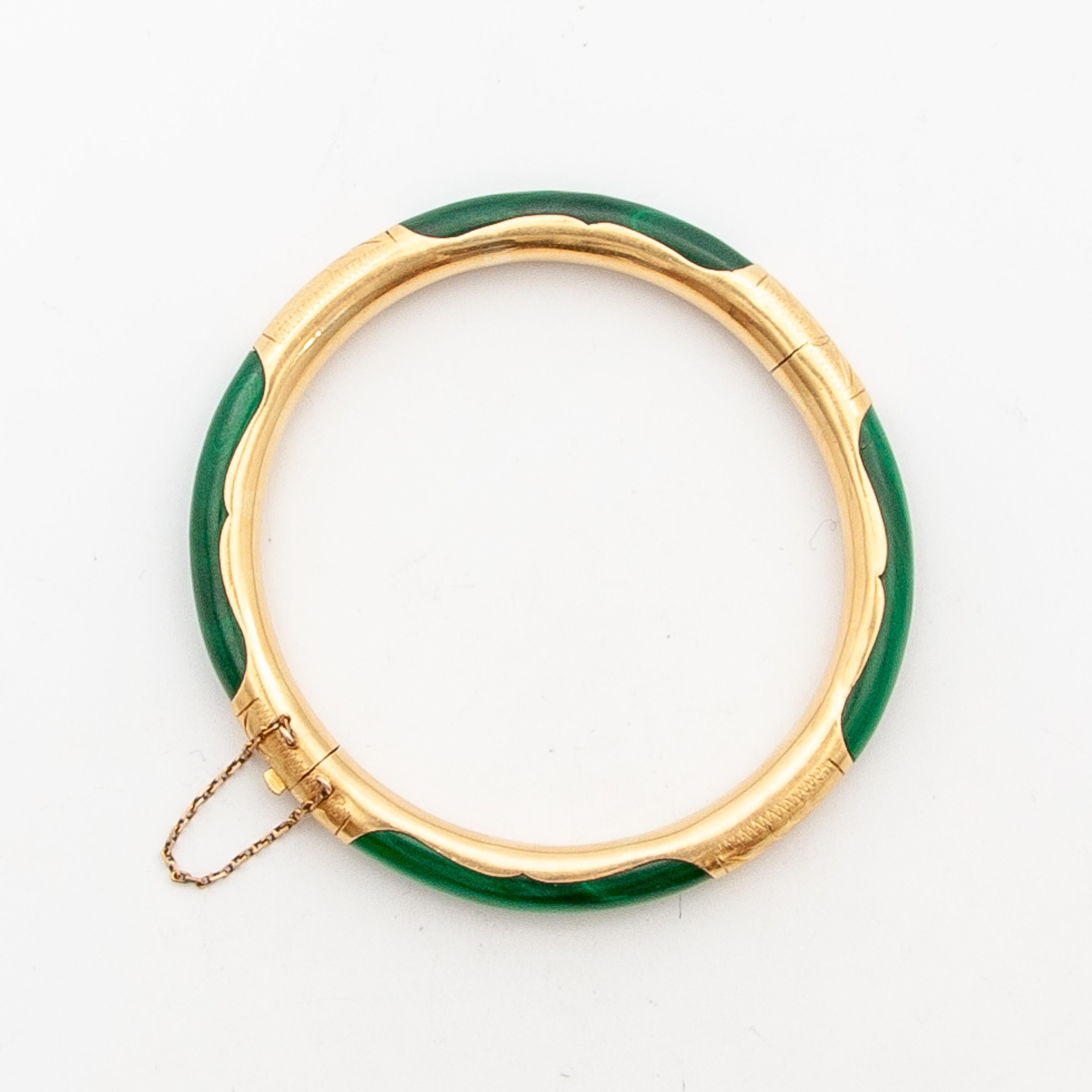 An 18 karat gold etched Malachite hinged bangle bracelet. This lovely bangle features a smooth round polished stone with mixed green tones. The 18 karat gold engraved foliage compartments accentuate the Malachite sections. The bangle bracelet is