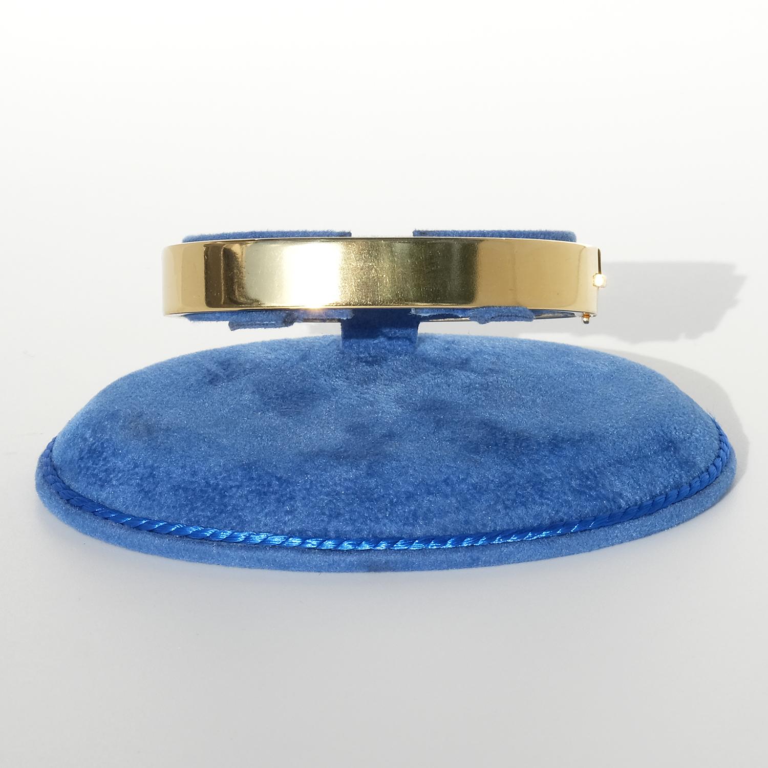 This 18 karat gold fixed bracelet has an elegant, slightly oval shape, giving it a substantial and luxurious feel on the wrist. Its smooth, polished surface emphasizes the bracelet’s minimalist sophistication, allowing the quality of the gold and