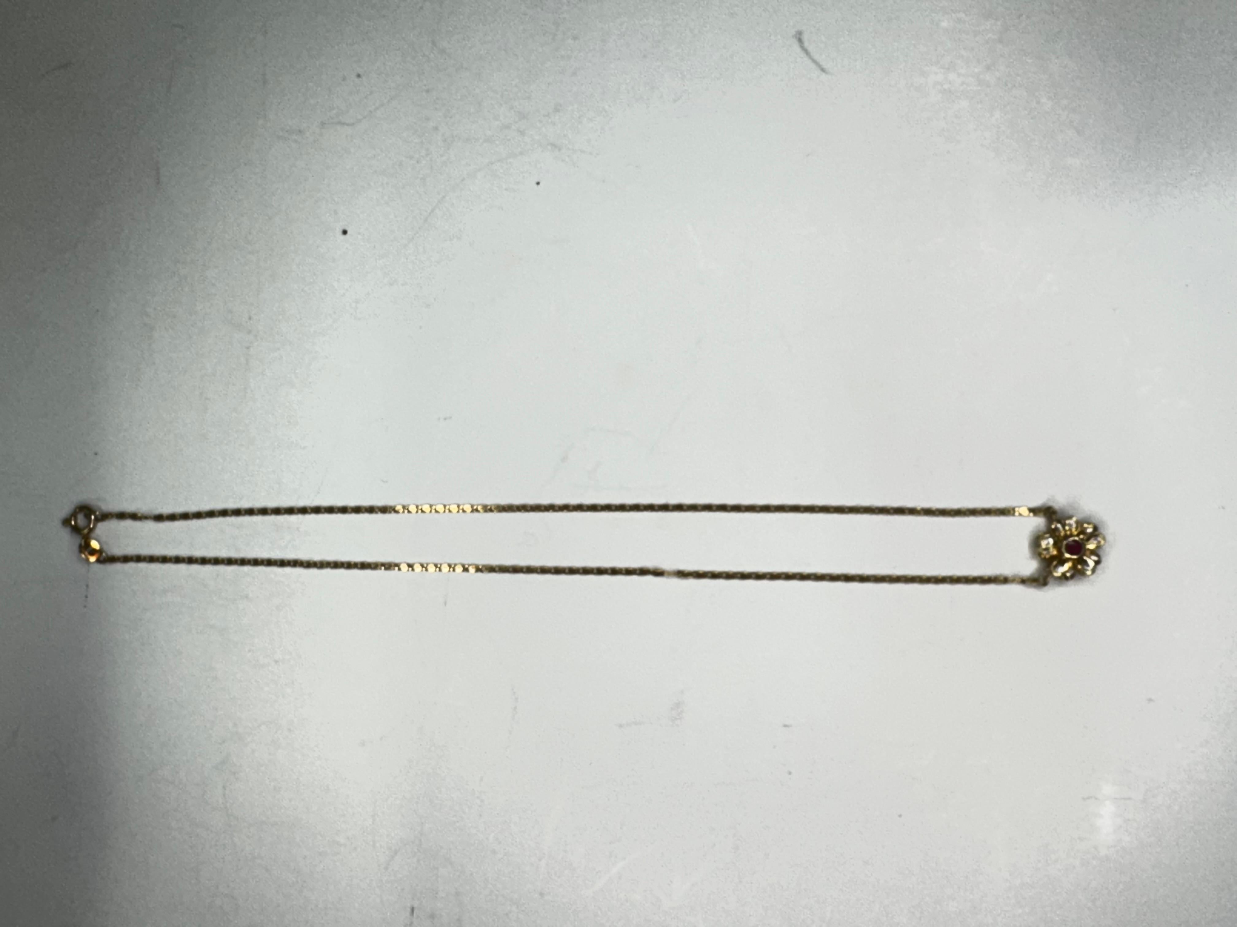 Cet élégant collier à pendentifs en forme de fleur est réalisé en or 18 carats et présente un magnifique design qui allie charme classique et détails raffinés. Au cœur du pendentif se trouve un rubis vif, rayonnant d'une riche couleur rouge et d'une