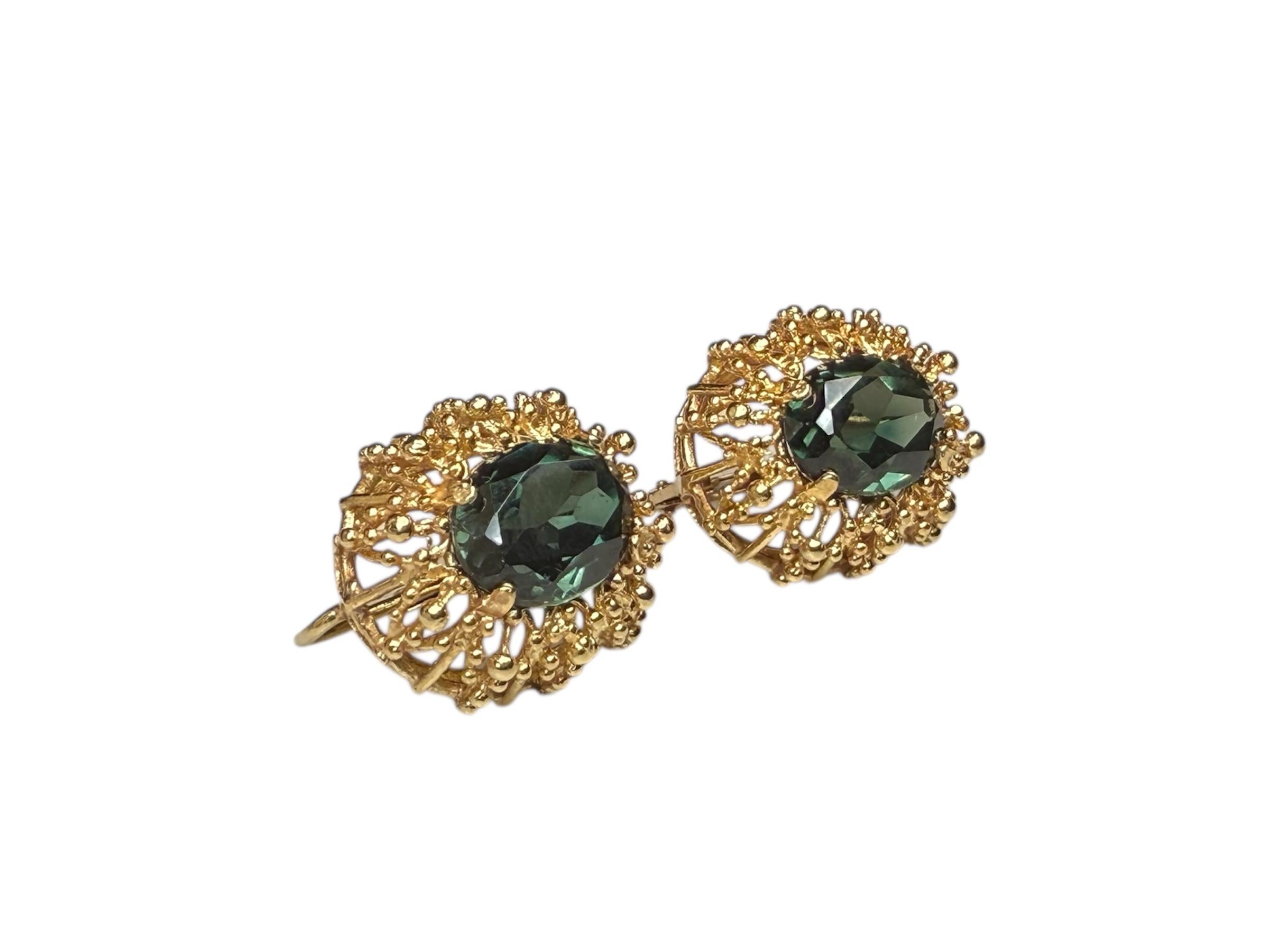 Si tratta di un paio di orecchini di topazio in oro 18 carati. Raffigura un topazio verde scuro sfaccettato di forma ovale (10,2 x 7,7 x 5,91) montato in una montatura d'oro e circondato da una corona di spighe con piccole perline. Gli orecchini