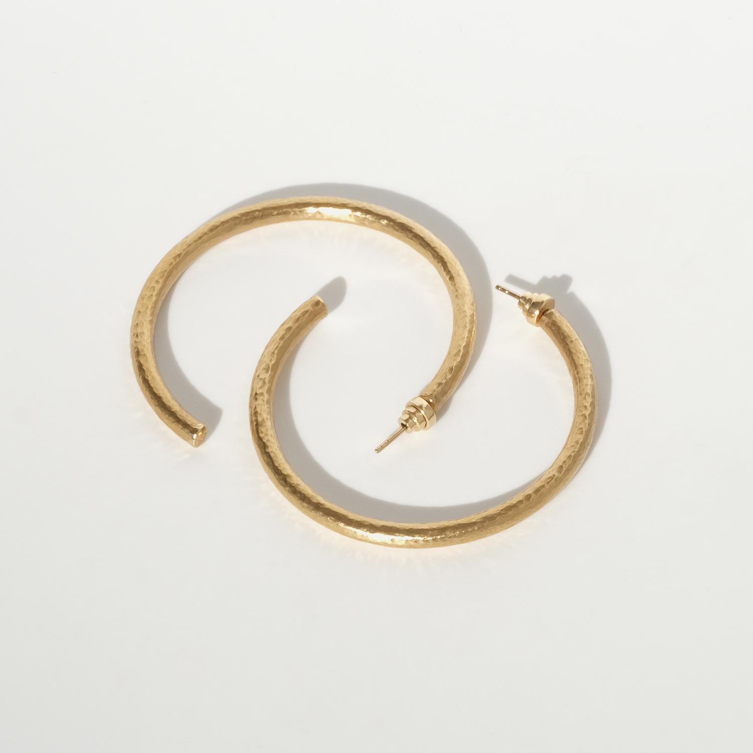 Questi orecchini vintage sono realizzati in oro a 18 carati e hanno la forma di grandi cerchi aperti con un profilo pulito e arrotondato. La superficie ha una texture finemente martellata che ammorbidisce il metallo e conferisce all'oro una
