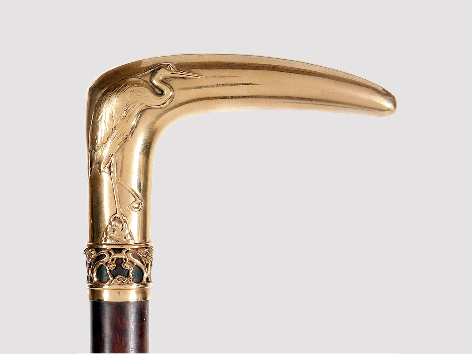 Bastón enjoyado de oro de 18 quilates. Uno de los lados del pomo presenta la imagen en relieve de una garza, cuyo cuerpo se adapta naturalmente a la forma de la empuñadura. El pájaro se coloca con una sola pata sobre una pequeña roca apoyada en el