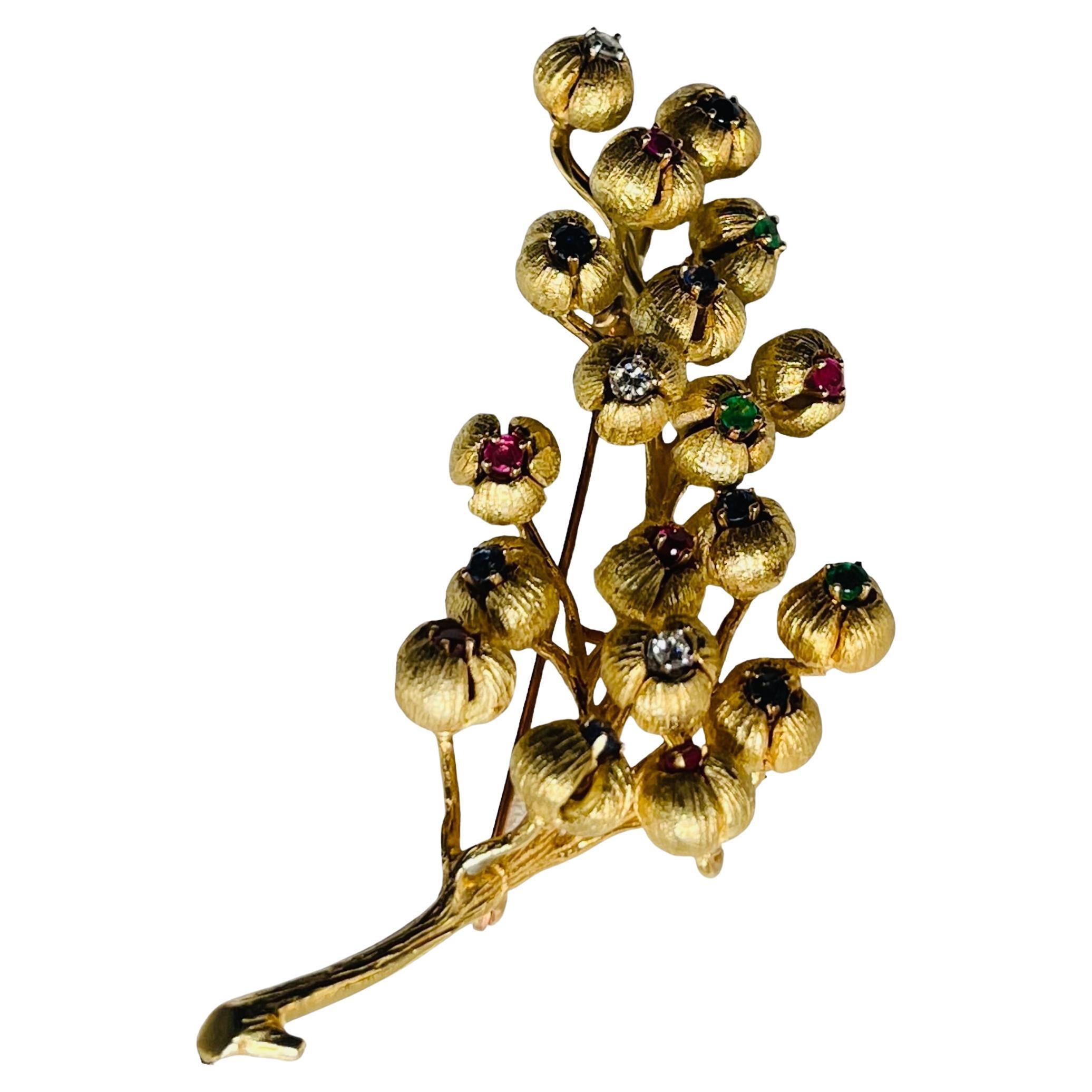 This is a 18K yellow gold multi gemstones diamonds brooch. It depicts a long branch of Lilies of The Valley flower buds with multiples small branches of buds of the same flower embellished with round cut six rubies, seven sapphires, three emeralds
