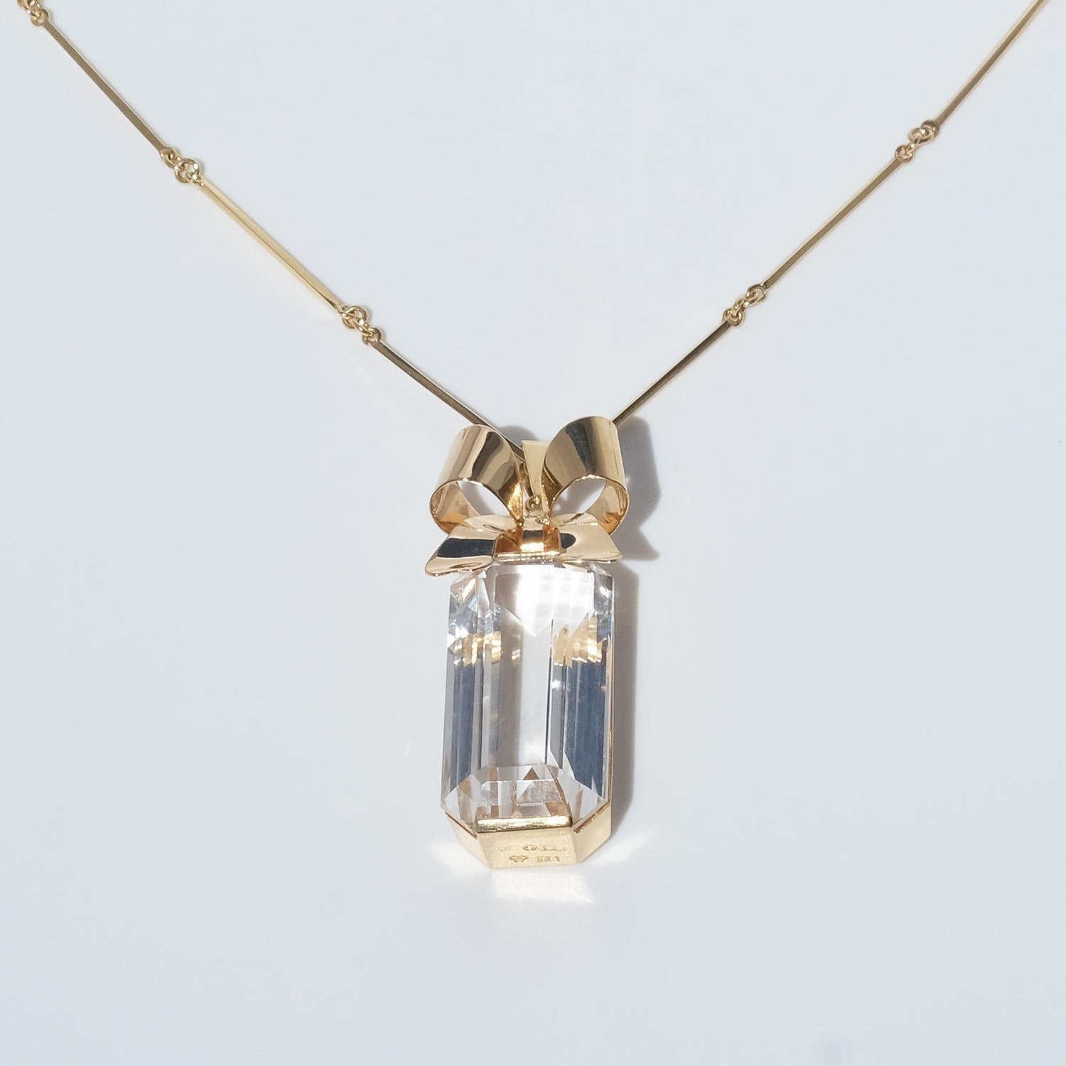 Questa collana in oro 18 carati e cristallo di rocca presenta le caratteristiche tipiche di questo periodo, come la catena ad anello e a barretta e il ciondolo dalle forme geometriche rettilinee, la superficie lucida e il cristallo di rocca dal