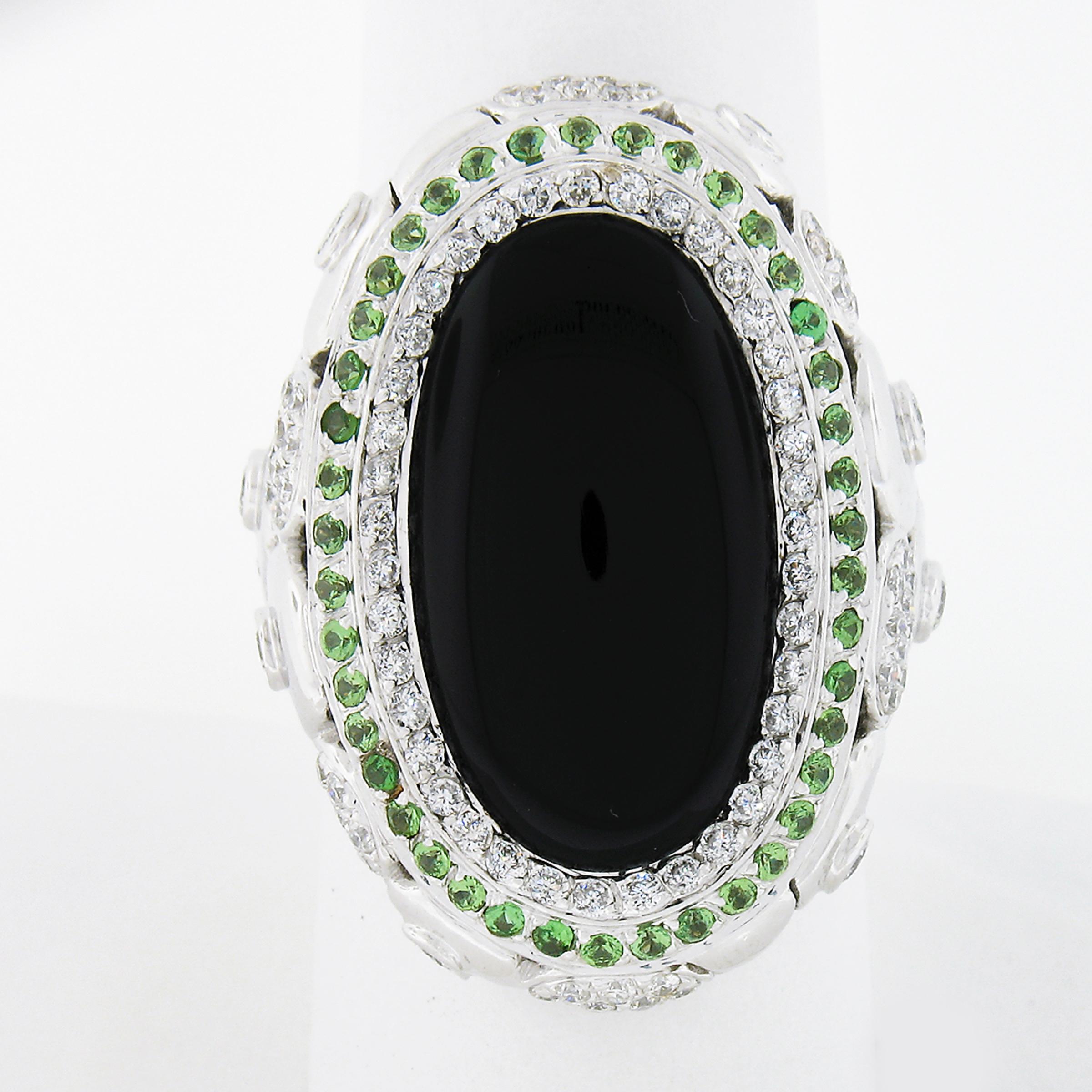 This beautiful statement ring is crafted in solid 18k white gold and features a large black onyx solitaire with fine diamond and Tsavorites accents throughout. The oval cabochon cut onyx shows a nice black color with a polished finish and is further