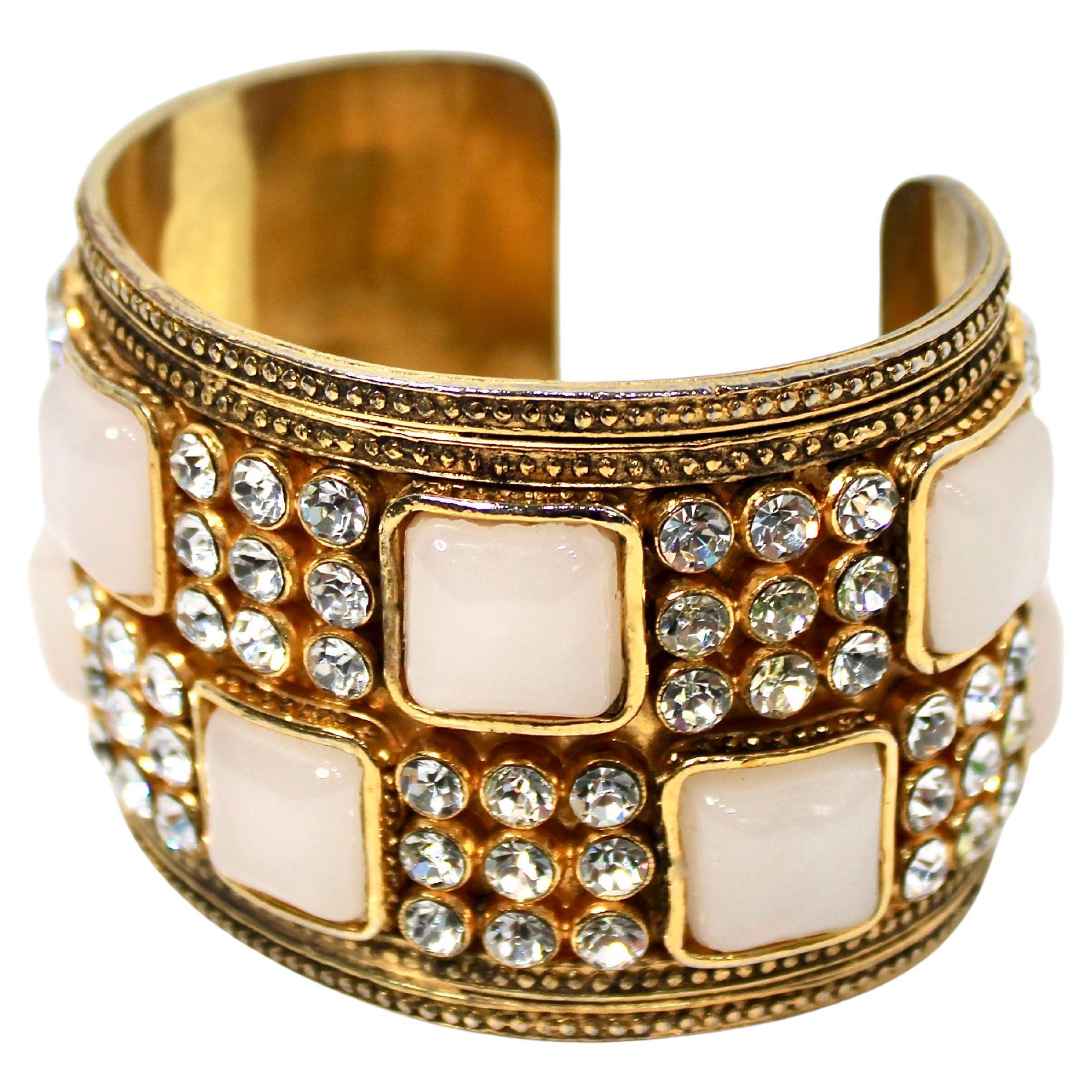 Este impresionante Chanel  La pulsera brazalete con piedras y cristales bañada en oro de 18 quilates es un accesorio impresionante diseñado para realzar cualquier conjunto. Adornado con luminosas piedras de fantasía blancas y brillantes cristales,