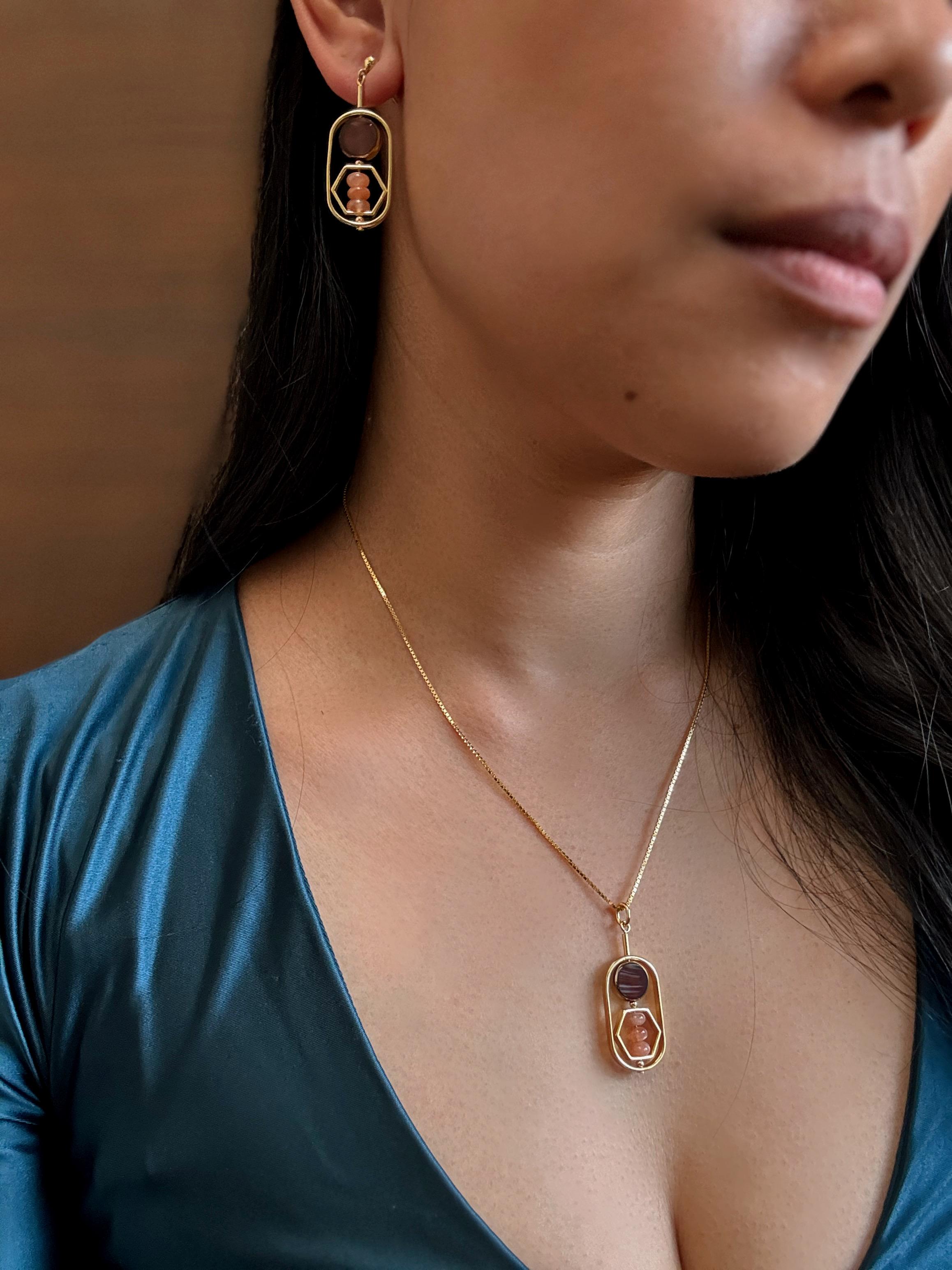 La modella indossa una catena da 18 pollici. 

Il ciondolo è composto da pietre del sole e perline di vetro tedesco marrone marmorizzato di nuova produzione, incorniciate da oro 24 carati. La maggior parte delle perline utilizzate nella collezione