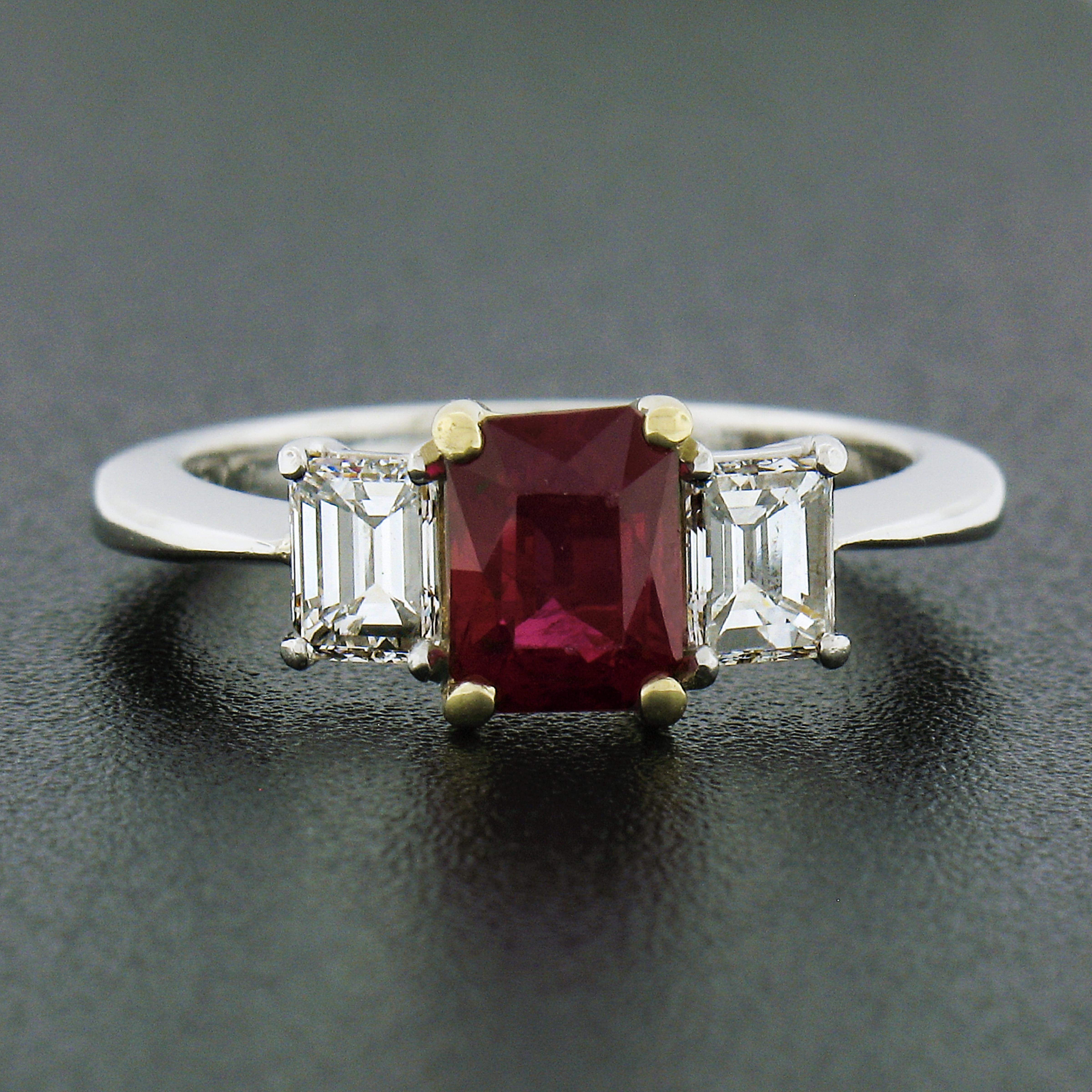 You are looking at a classically styled ruby and diamond three stone engagement ring crafted in solid platinum, and features a gorgeous, GIA certified, ruby solitaire neatly prong set at the center in a yellow gold basket setting. This center stone