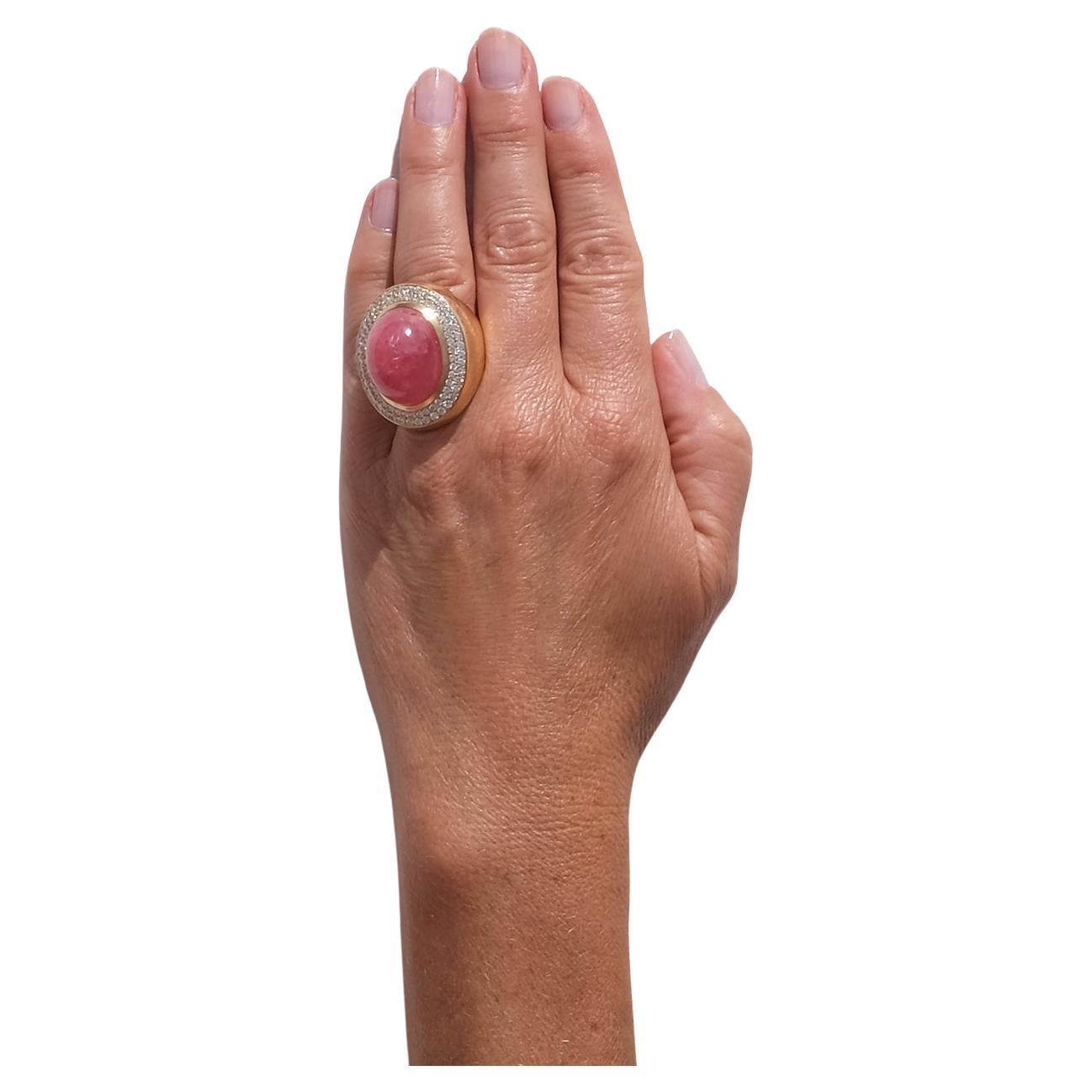 Audacieuse et sculpturale, cette bague vintage en or 18 carats présente une rhodochrosite de taille cabochon proéminente, richement veinée et pleine de caractère. La pierre est sertie d'un chaton et entourée d'un cadre serti de deux rangées de