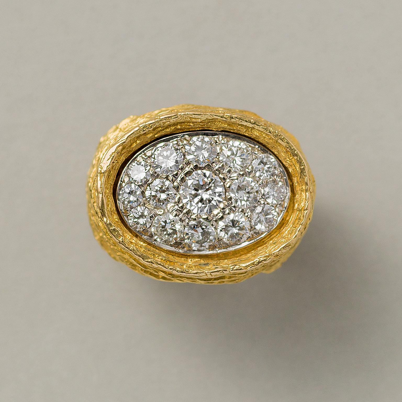 An 18 carat gold and diamond ring, the front view is a large oval horizontally set over the finger pavé set with diamonds in white gold, nested in a higher yellow gold border which is part of shank with the curved horizontal ribs with texture,