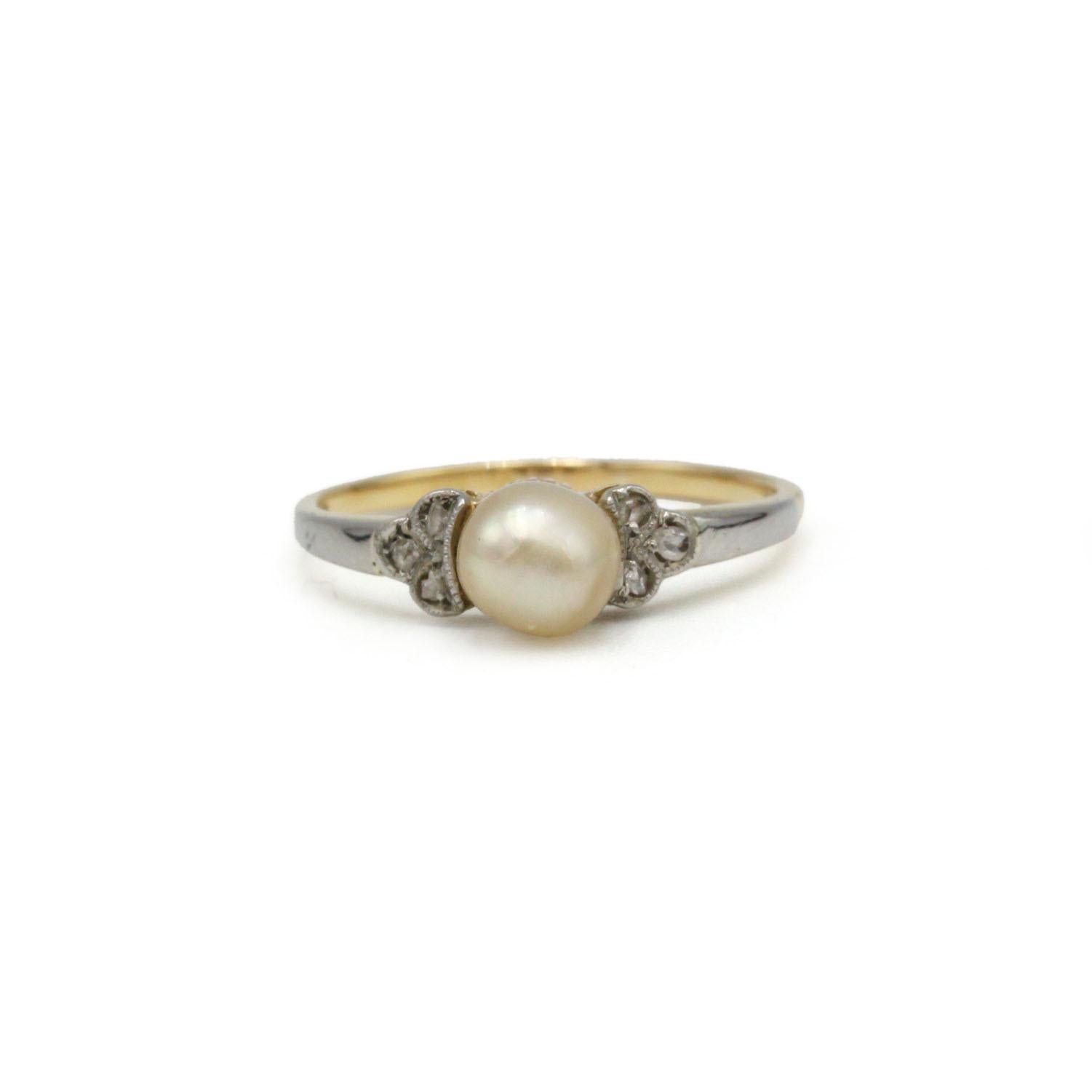 This delicate 18K gold ring features a pearl beautifully set at the center, framed by two clusters of old-cut diamonds on each side. The contrast between the warm yellow gold band and the white gold shoulders enhances the soft glow of the pearl,