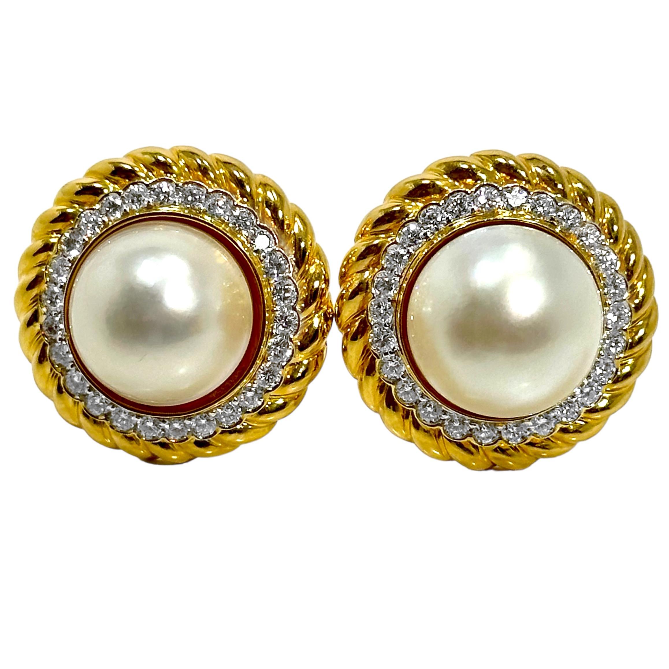 A stunning pair of clip-on earrings in 18K yellow gold, centered around two 16mm mabe pearls. A halo of round brilliant cut diamonds framed in gold surround the mabe pearls giving the appearance of a scalloped edge. The scalloped area is then