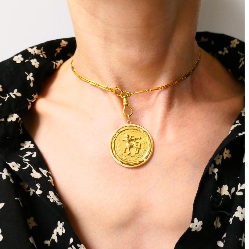 Un ciondolo vintage dello Zodiaco in oro 18k e una collana con catena d'orologio in oro 10k.
Il ciondolo rotondo ha una raffigurazione in rilievo dell'arciere del Sagittario, simbolo di avventura e indipendenza. L'arciere è centrato all'interno di