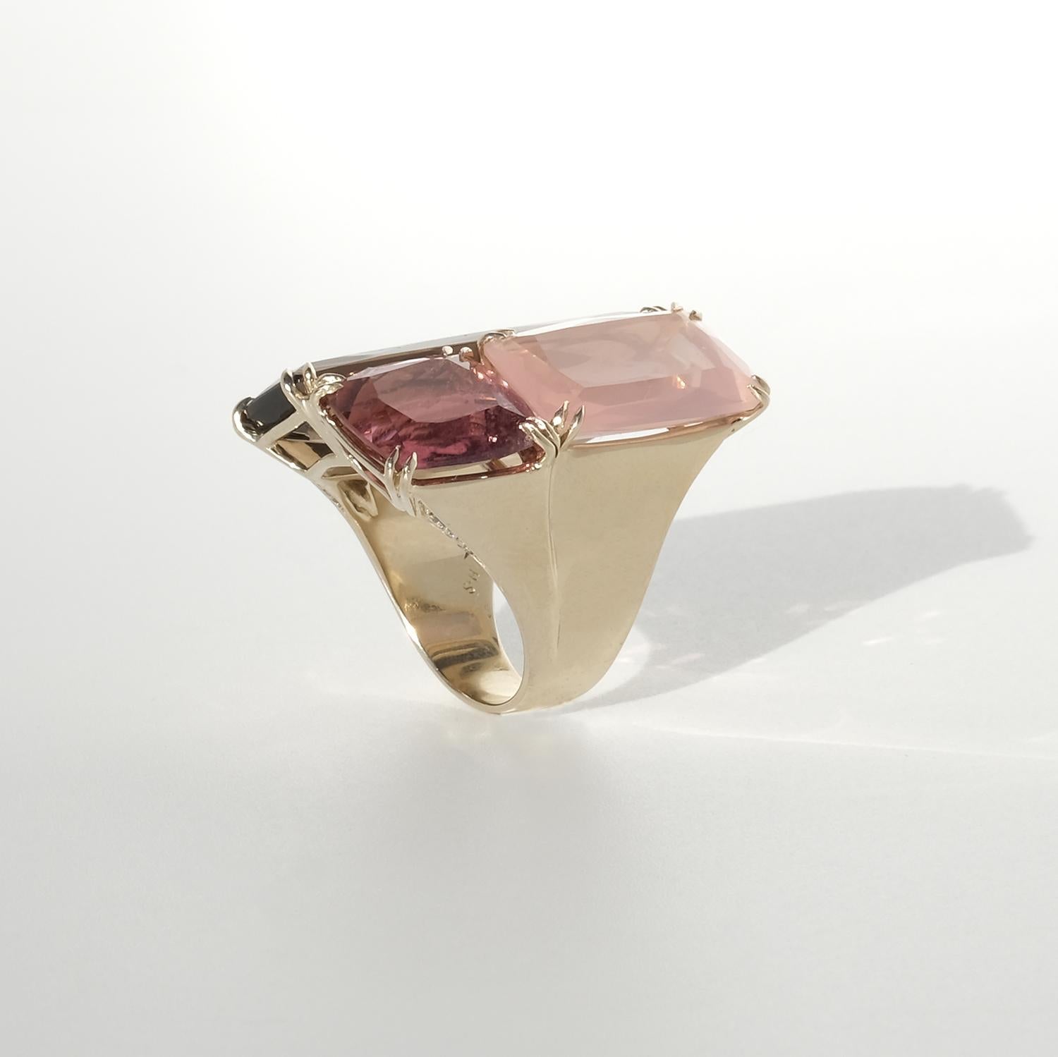 Dieser Ring ist aus 18 Karat Gold gefertigt und zeigt eine einzigartige Anordnung von Rauchquarz, Turmalin und Rosenquarz im Stufenschliff. Die farbigen Steine sind in einem leichten Winkel angeordnet, wie ein schräges Dach, mit unterschiedlichen