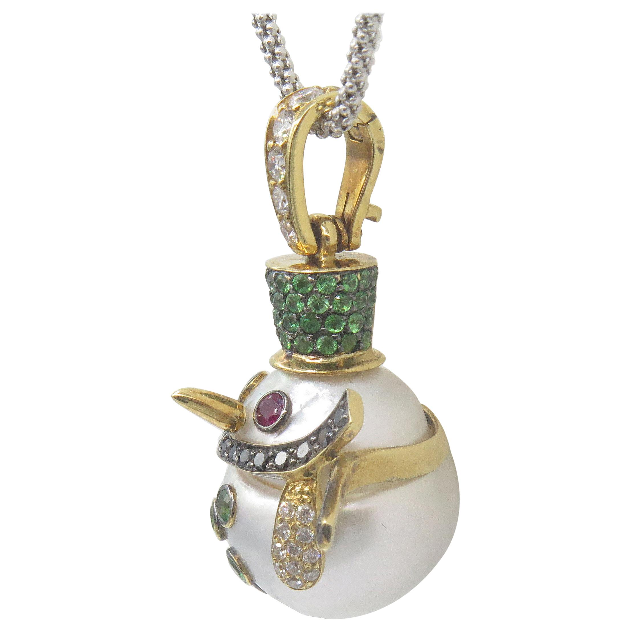 This whimsical south sea pearl snowman is dressed up in styles with a tsavorite garnet hat, buttons ,ruby eyes, black diamond scarf and white diamond gloves  All set in 18k yellow gold, dangling from a white diamond bale set on a 18' white gold