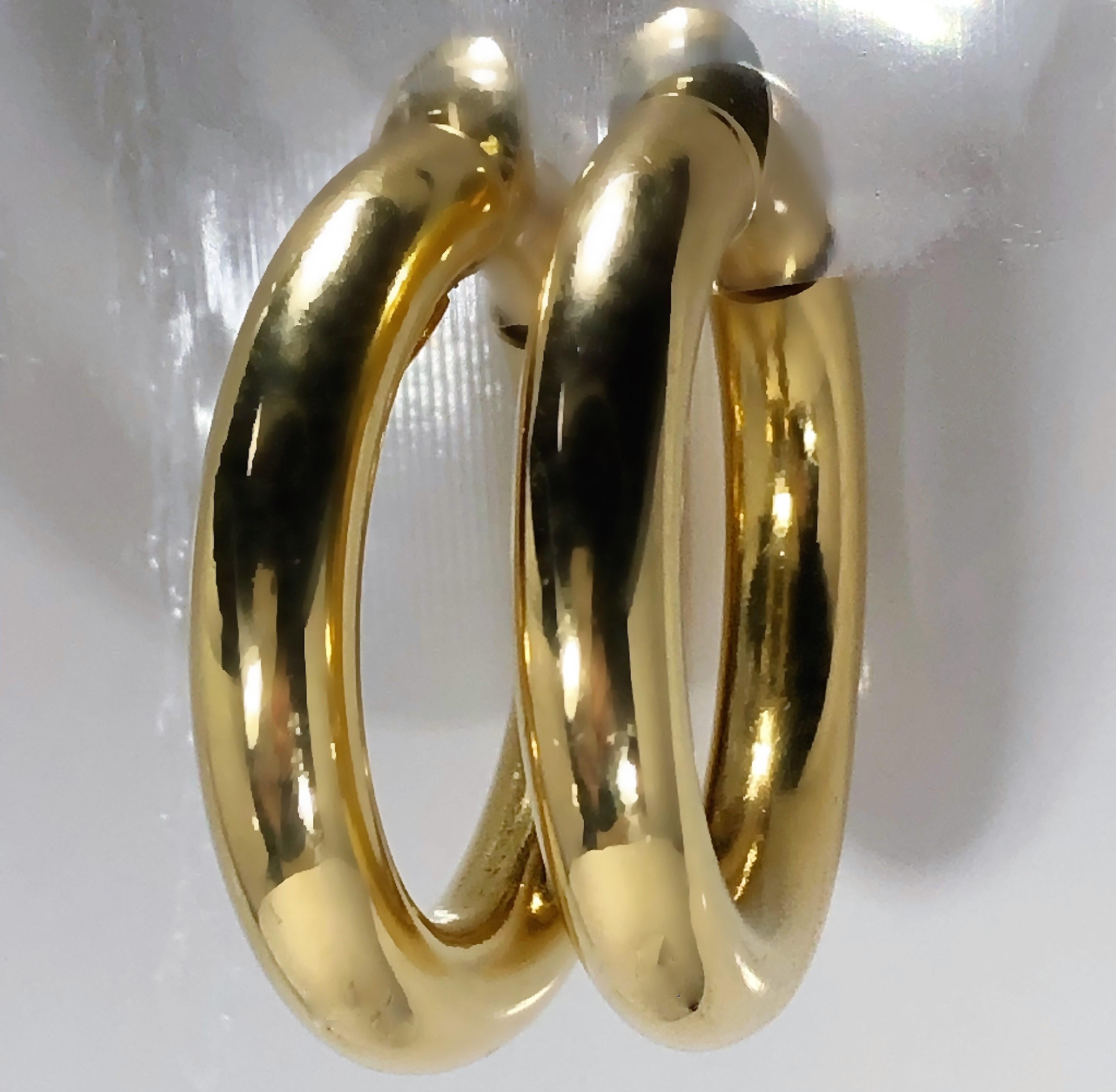 This lovely pair of 18k yellow gold high polish, classic hoop earrings measures 1 3/16 inches in diameter by 3/16 inches thick. Their ingenious spring loaded clasp mechanism makes them ideal for ladies who want to wear hoops but do not have pierced