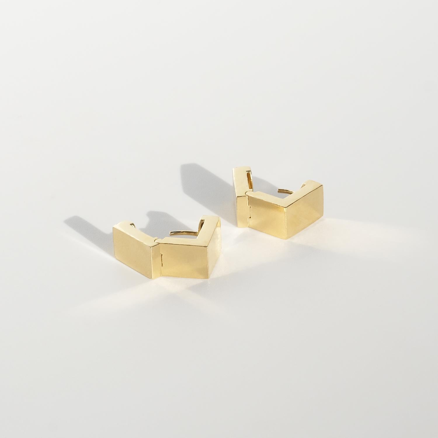 These 18 karat gold earrings are sleek, square-shaped huggies with a minimalist design. Each earring features a hinged construction, making them exceptionally easy to put on. They secure with a simple threaded post that clicks into place, providing