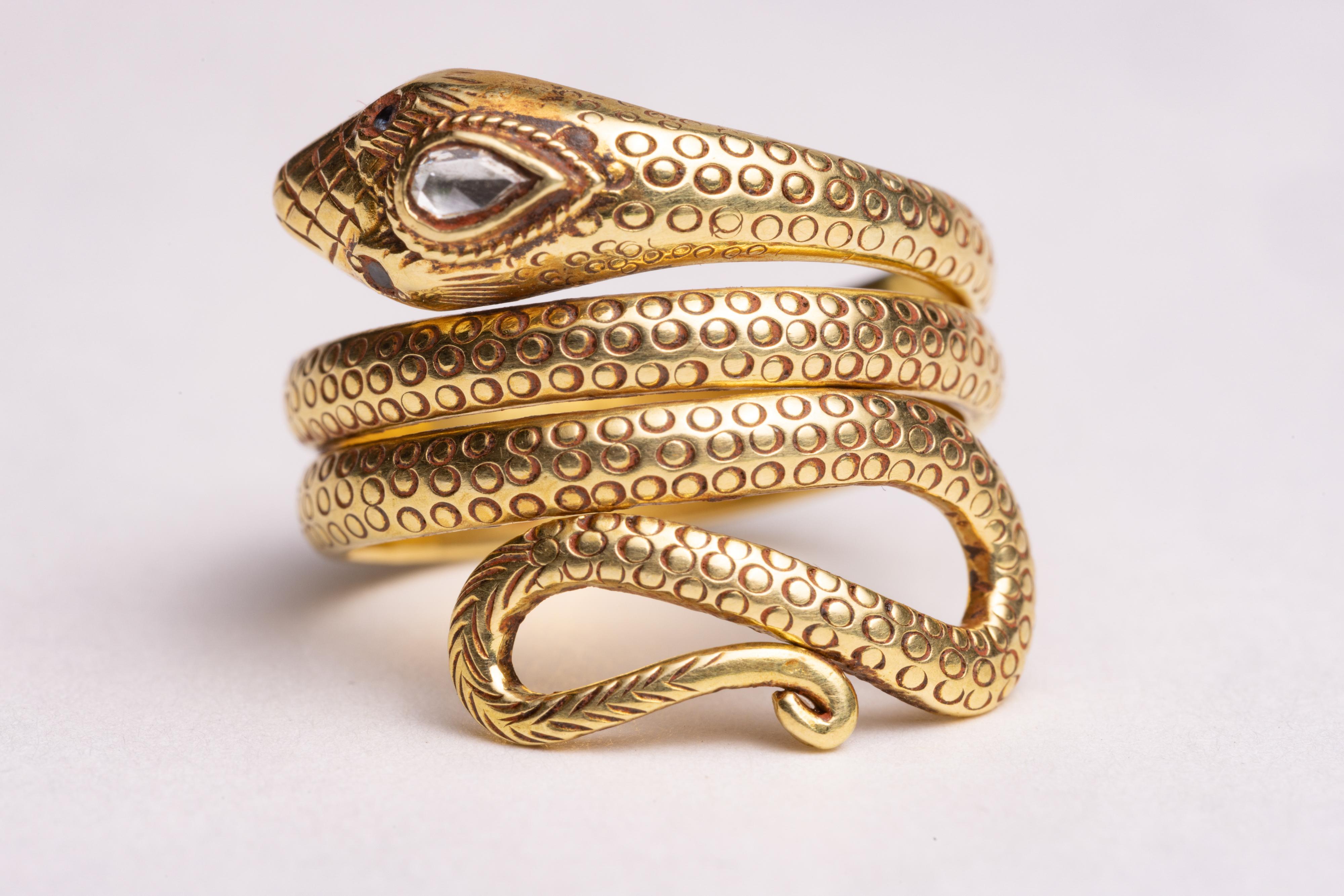 An unusual and stunning 18K gold coiled snake ring with fine hand-tooled workmanship along the band depicting the scales of the snake.  It features a faceted, pear-shaped diamond at the third eye and small round faceted sapphires for the eyes.  Ring