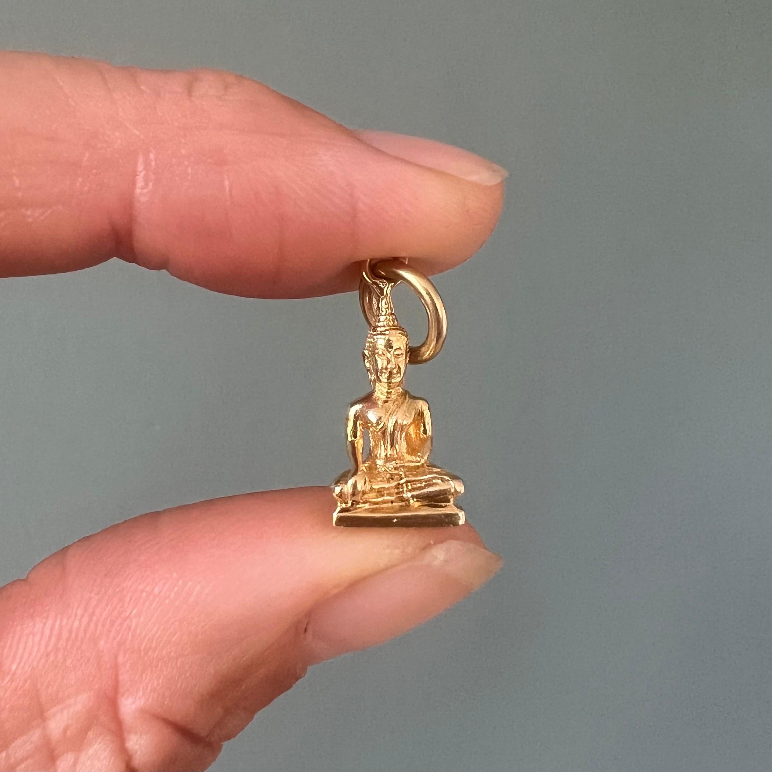 Un charme Buddha vintage finemente lavorato in oro giallo massiccio 18 carati, modellato in stile tibetano. La figura raffigura un sereno Buddha seduto in posizione di meditazione, con indosso le tradizionali vesti monastiche e coronato da un