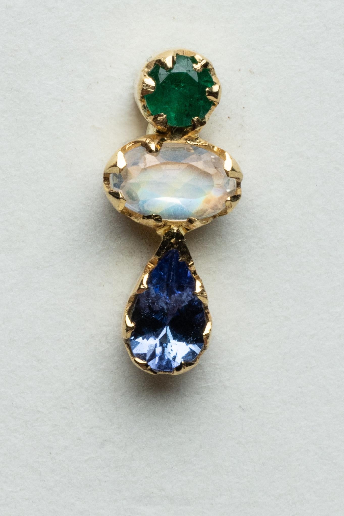 An elegant trio of gemstones comprise this pair of bezel-set stud earrings in 18K gold.  The top stone is a round, faceted emerald of .20 carats; the middle is a faceted, oval rainbow moonstone of .46 carats and the third is a pear-shaped, faceted