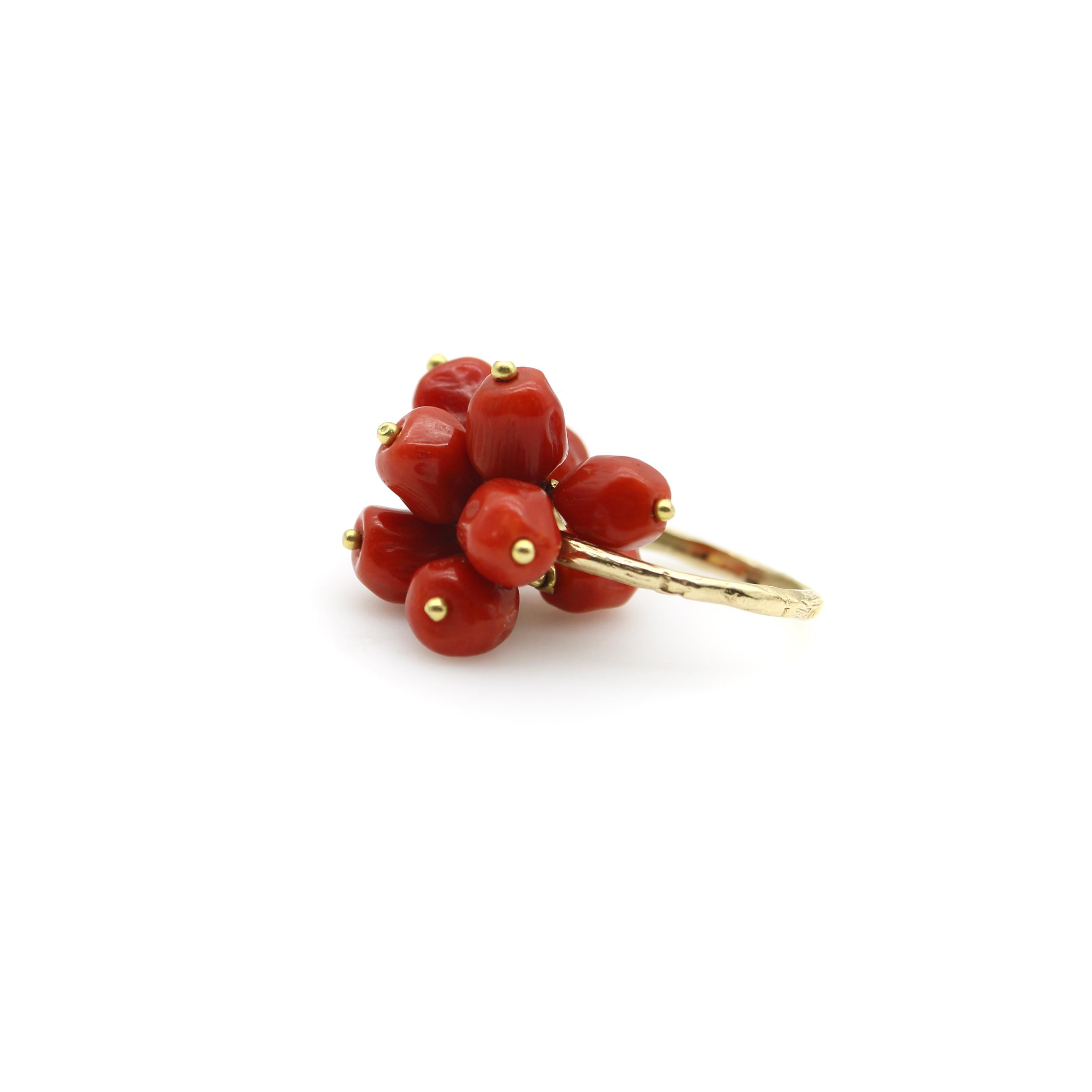 This vintage 18k gold ring features a cluster of deep red, faceted coral beads. The beads are held in place by gold wire, wrapped around the top center of the band—allowing for movement. The ring is playful and perfect for summer, and the coral