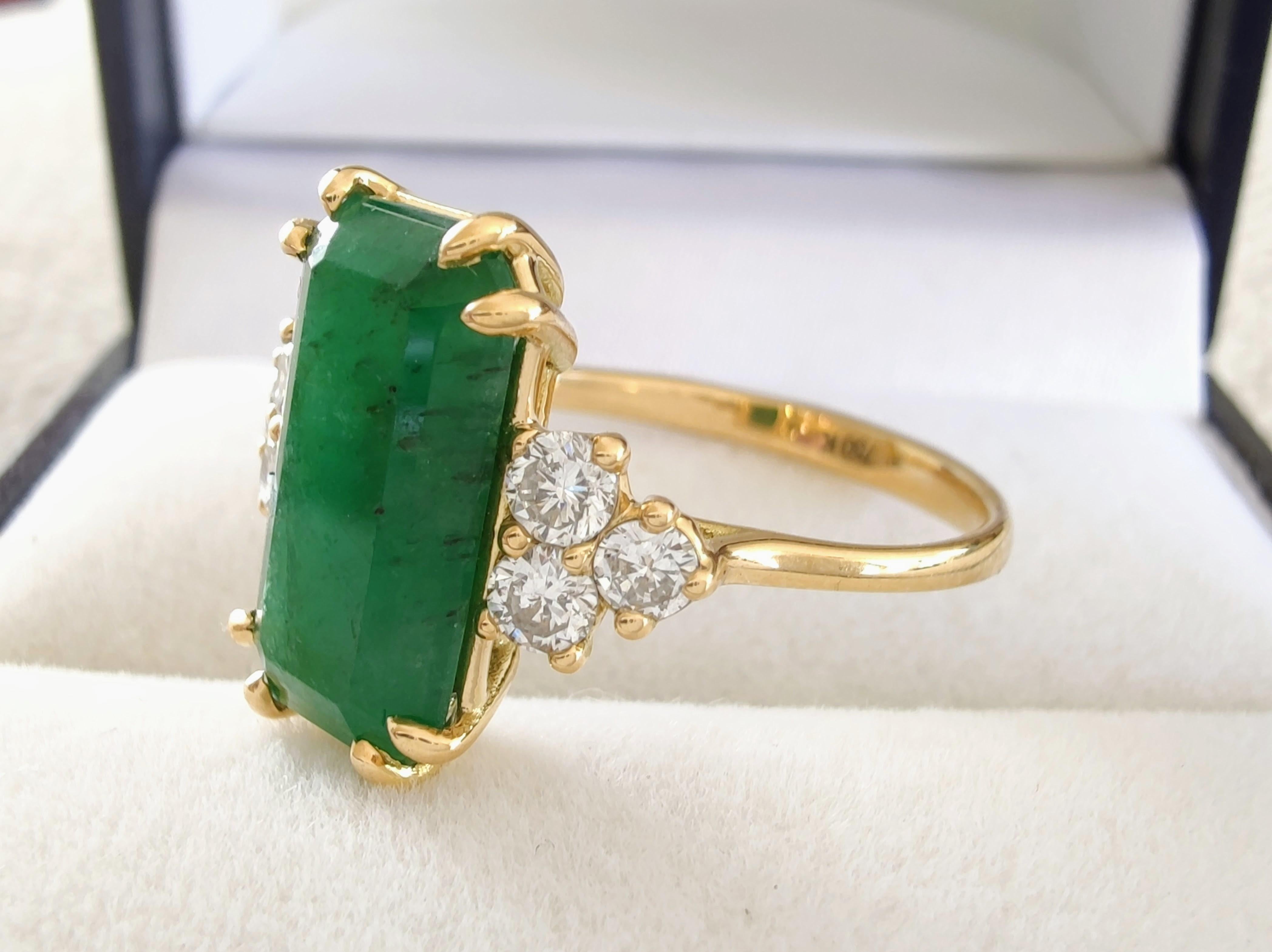 Entdecken Sie den ultimativen Ausdruck Ihrer Liebe mit unserem handgefertigten Smaragdring mit einem atemberaubenden Smaragd in der Mitte, flankiert von funkelnden Diamanten. Dieser exquisite Ring aus 18-karätigem Gold, der sich perfekt für