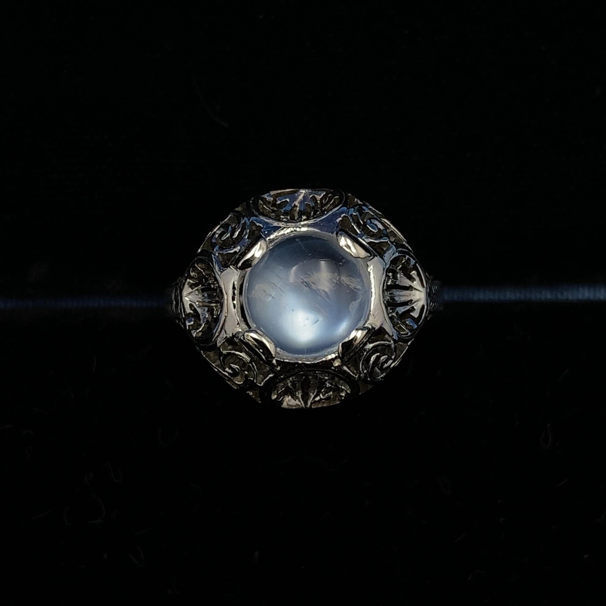 18k white gold filigree ring with a blue flash round moonstone. The mounting is Art Deco with hand piercing. The moonstone  weighs 1.66 carats and measures about 8mm. The ring fits a size 7 3/4 finger and weighs 3dwt. It dates from the 1920's.