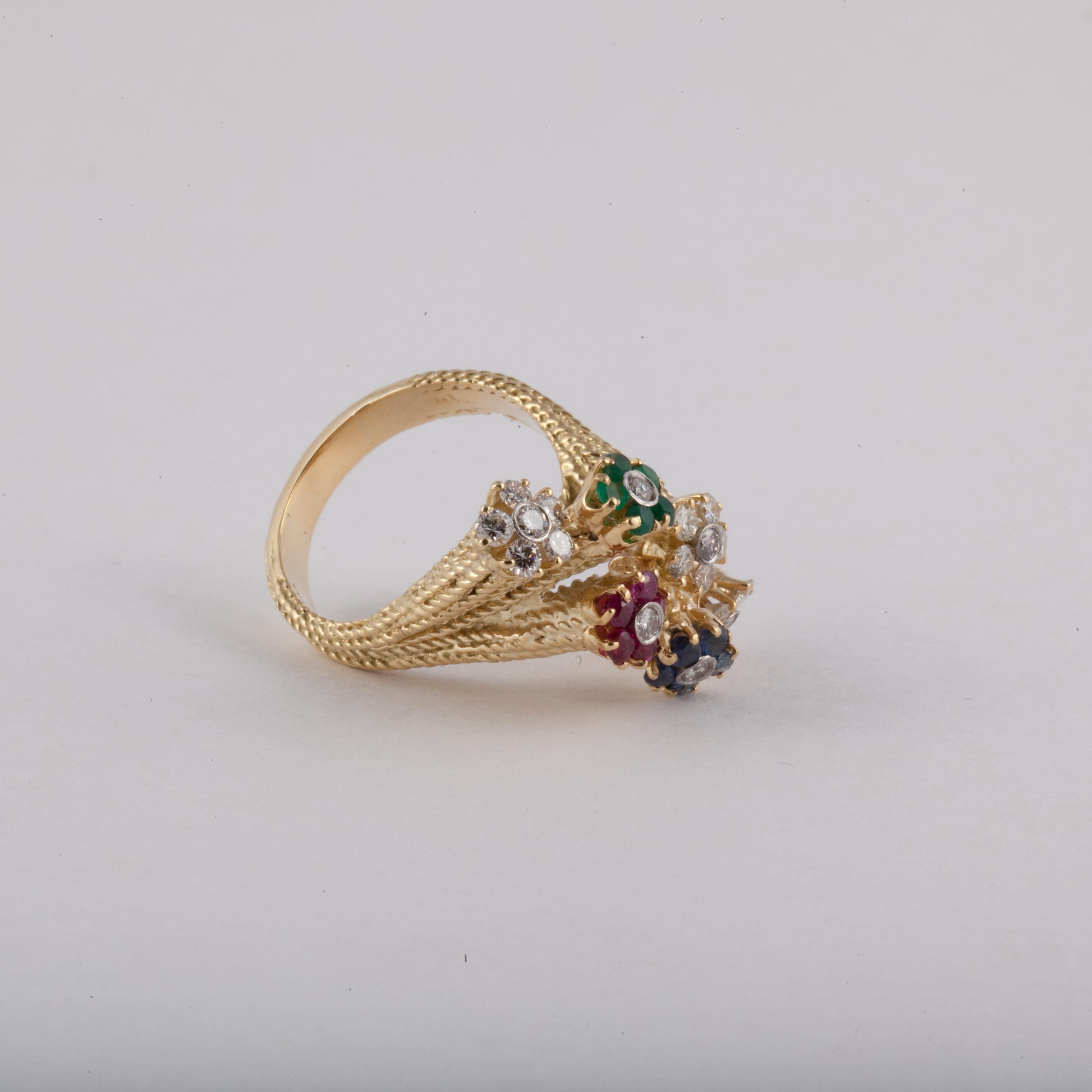 18K yellow gold ring featuring small flowers crafted in different gemstones, including diamonds, sapphires, rubies and emeralds.  The stems are textured.  Measures 1 1/4 inches long, 1/2 inch wide and stands 5/8 inches off the finger.  Circa 1970s.
