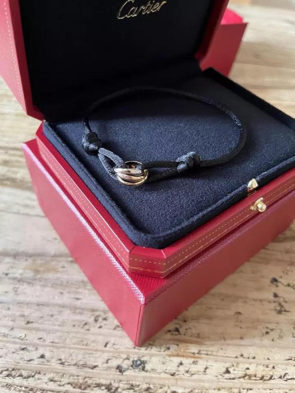 This is an authentic CARTIER 18K Gold Trinity Adjustable Cord Bracelet in Black. The bracelet is crafted of 18 karat Gold and features an adjustable silk cord with a trio of interlocking rings.
Trinity ring is a signature design of the Cartier
