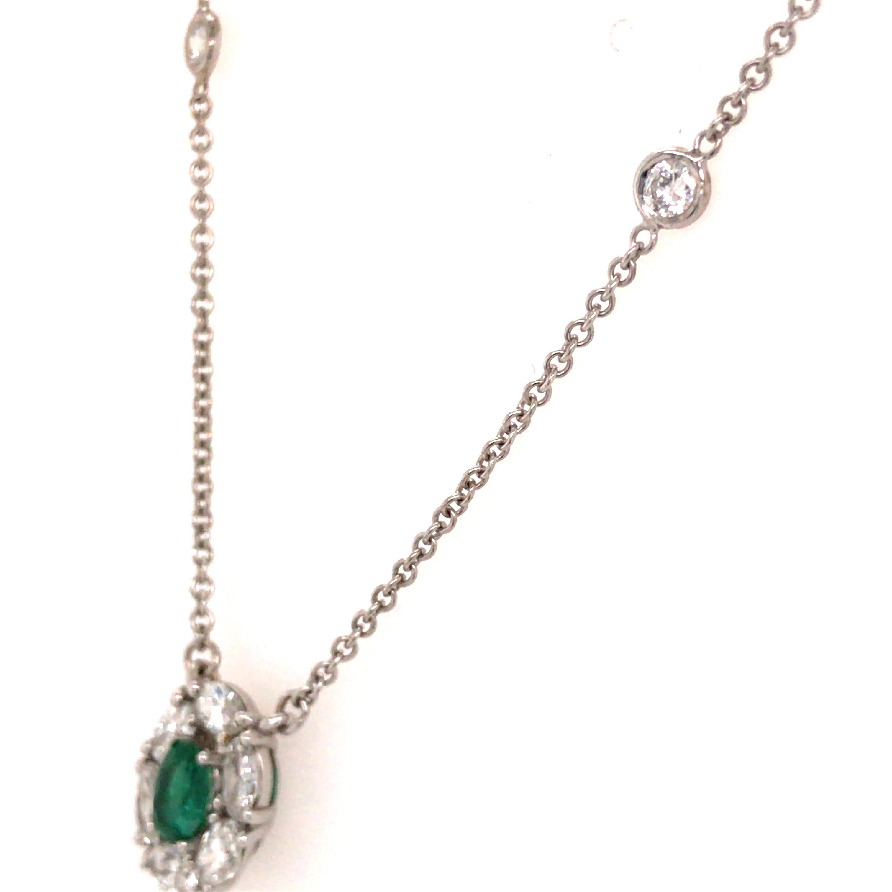 Oval Diamond and Emerald Pendant on a classic Diamond-by-the-Yard Necklace in 18K White Gold.  (6) Oval Shape Diamonds are expertly set in a halo around a .80 carat Oval Shape Green Emerald.  (6) Round Brilliant Cut Diamonds are bezel set in the