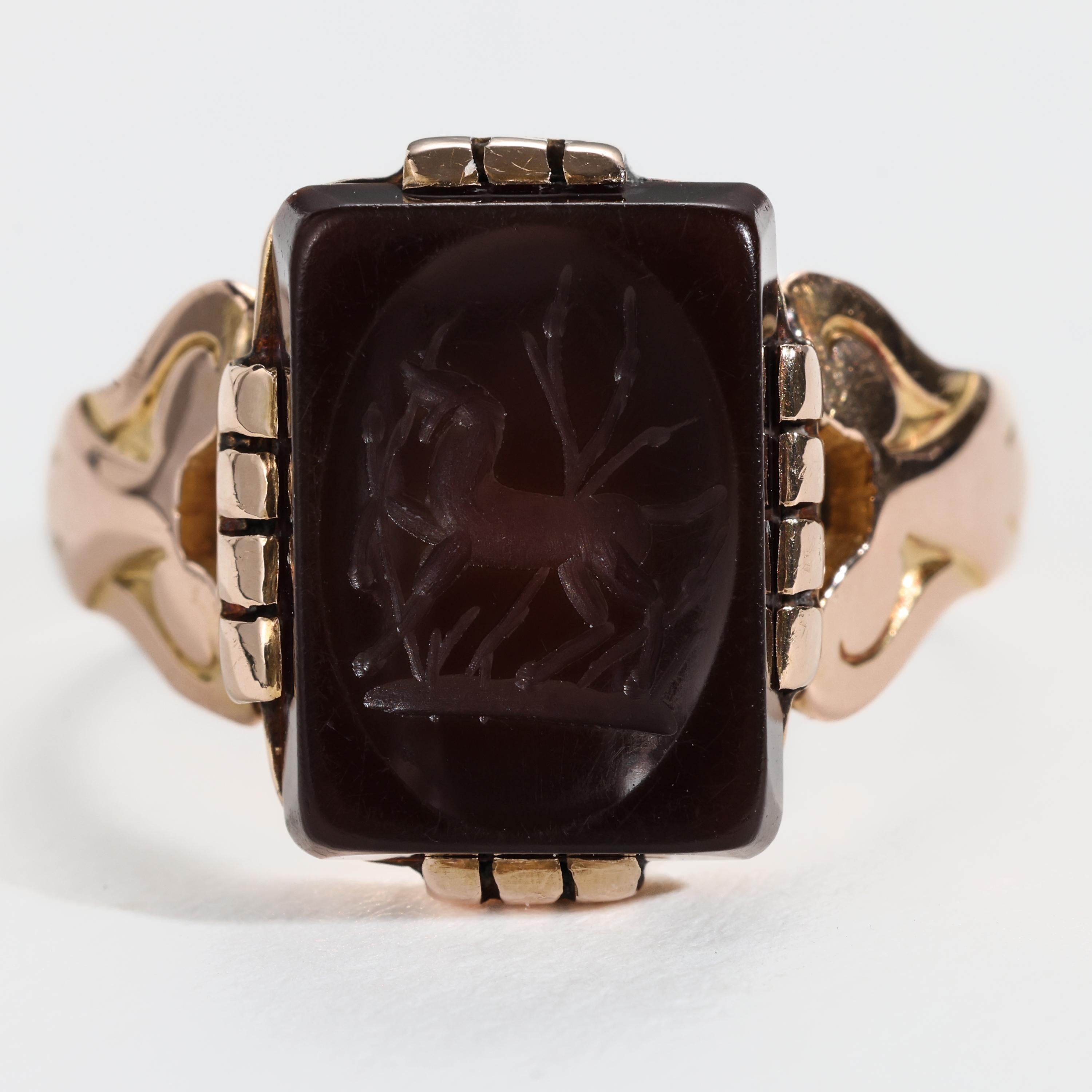 This late Georgian / early Victorian 18K rose gold ring holds a rectangular-cut deep brown sardonyx gemstone that has been artfully carved -or etched, rather- to depict a horse trotting among the tall grass. Rendered with superb artistry and skill,