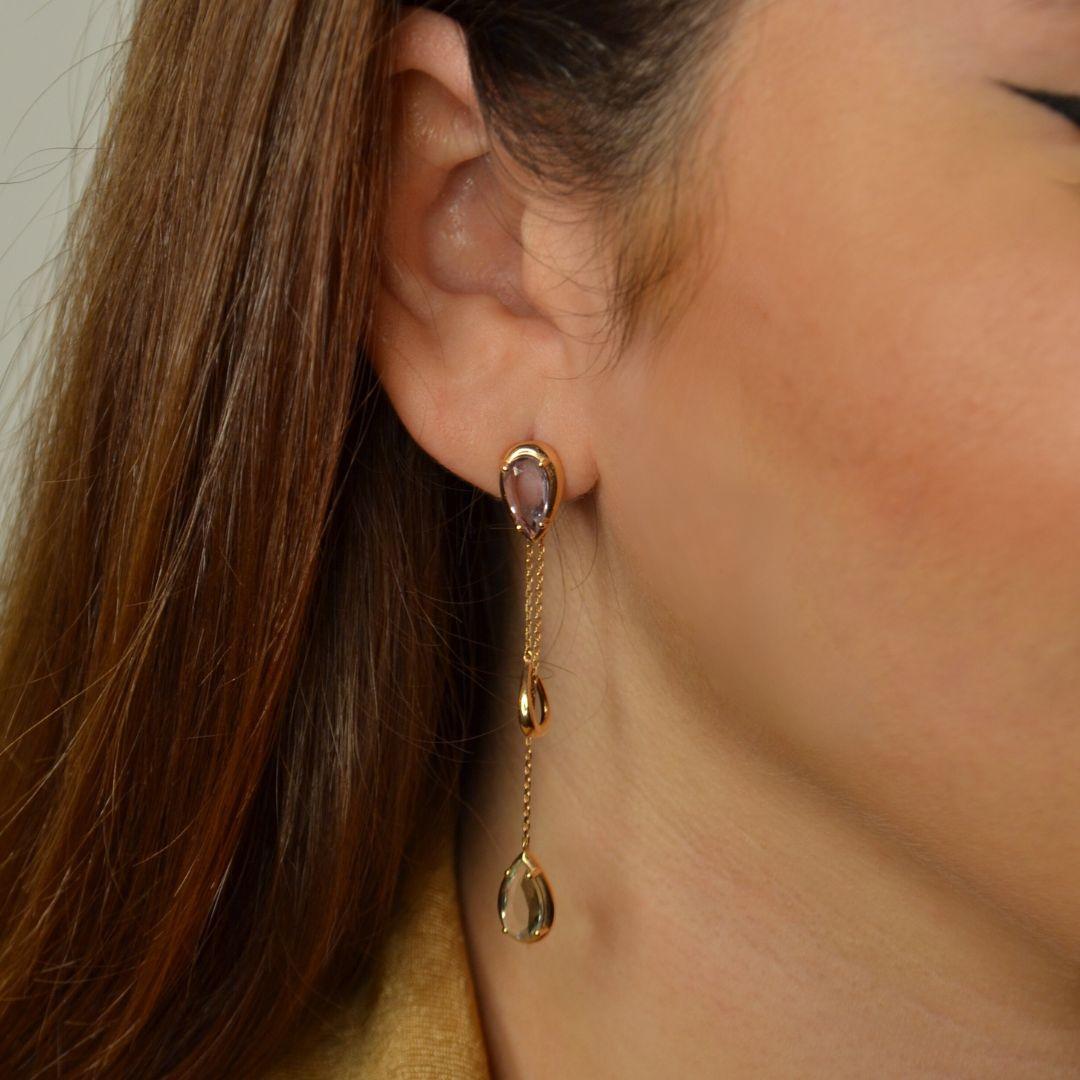 These elegant 18K rose gold drop-earrings feature a stunning combination of pear-shaped amethyst and prasiolite gemstones. The two gems are connected by delicate gold chains, creating a cascading effect that adds movement and sophistication. The top