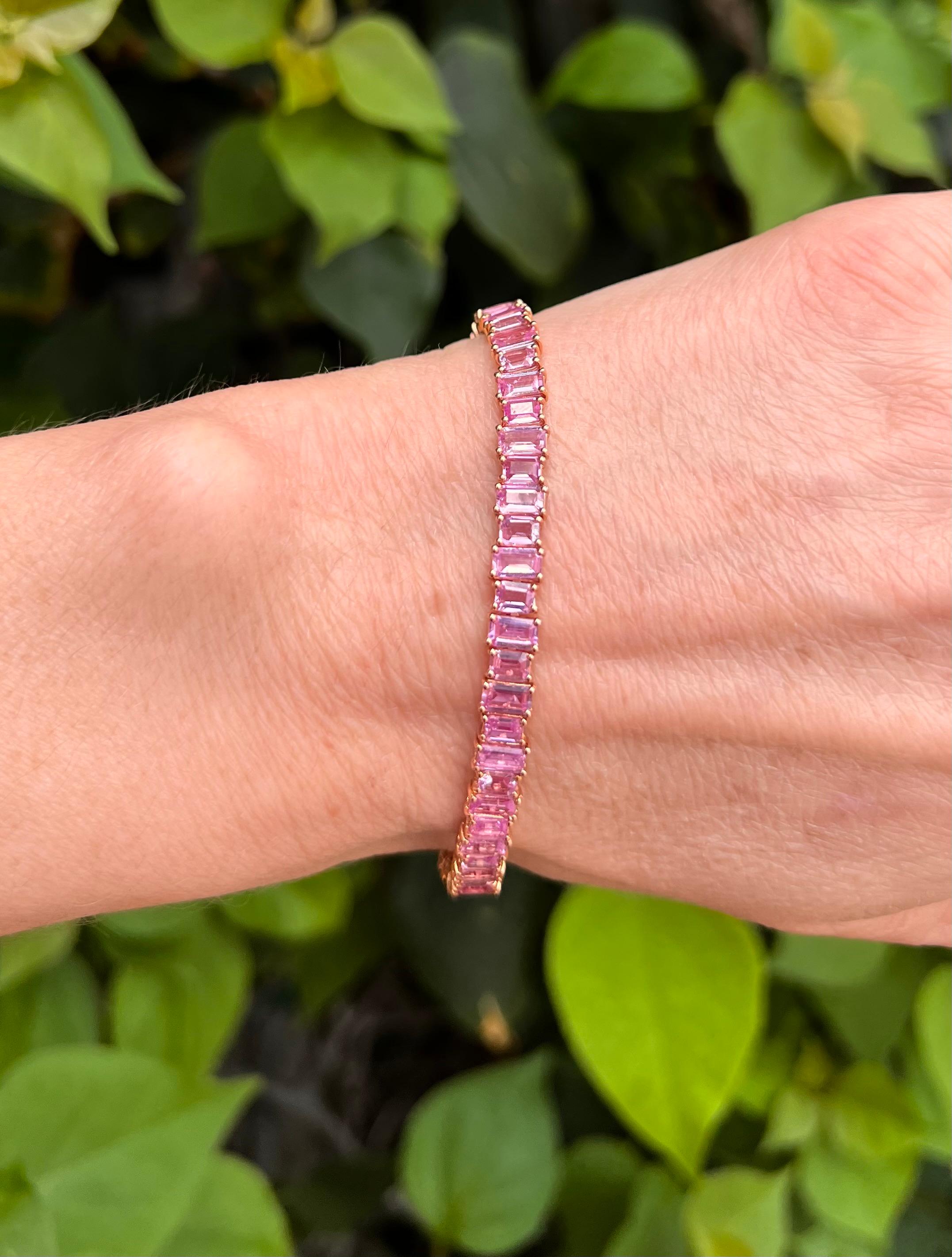 Vibrant pink sapphire line bracelet in 18k rose gold, featuring 55 rectangular, step cut, faceted pink sapphires, which are vertically set in a 'high-low' design, giving a dimension and sparkle to each stone.  Alternating 28 larger and 27 smaller