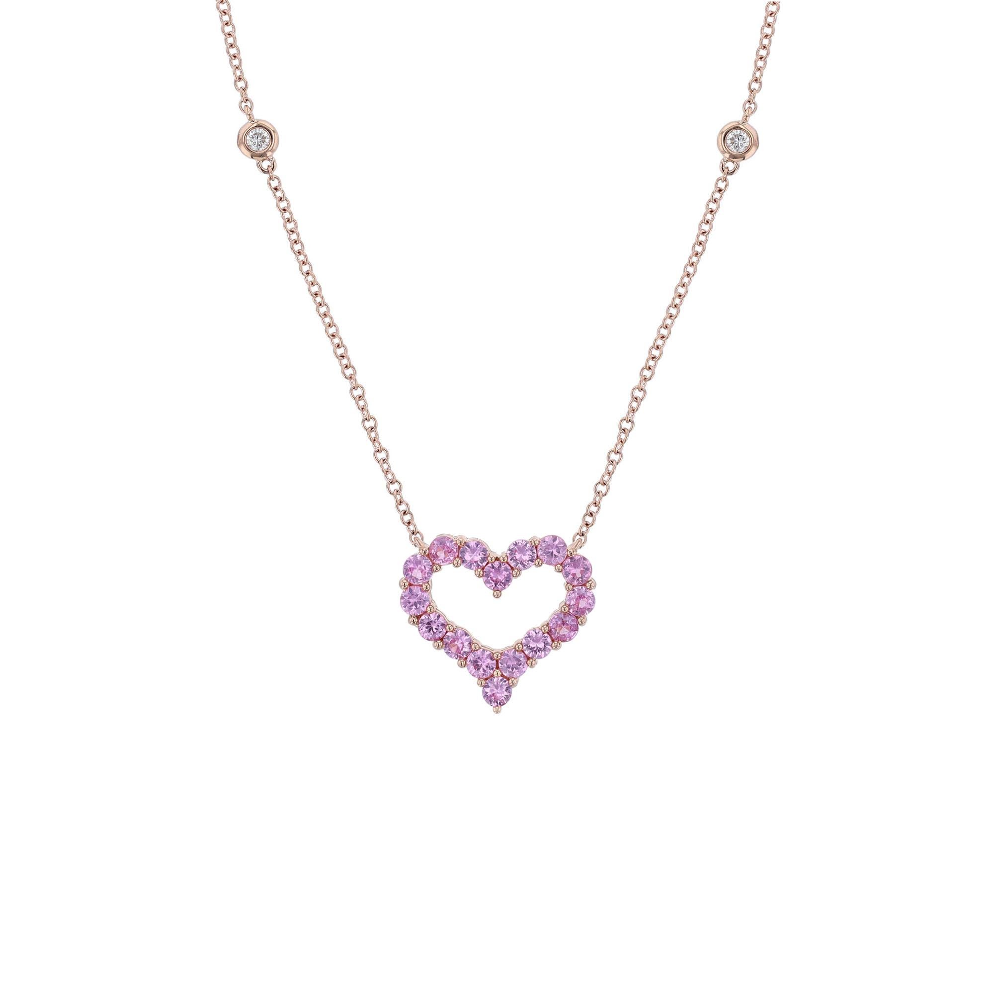 This pendant necklace is made in 18K rose gold. It features a heart shape pendant with 16 round cut, prong set pink sapphires. With 2 round cut, bezel diamond stations, and 2 pink sapphires bezel stations. The necklace has a color grade (H) and