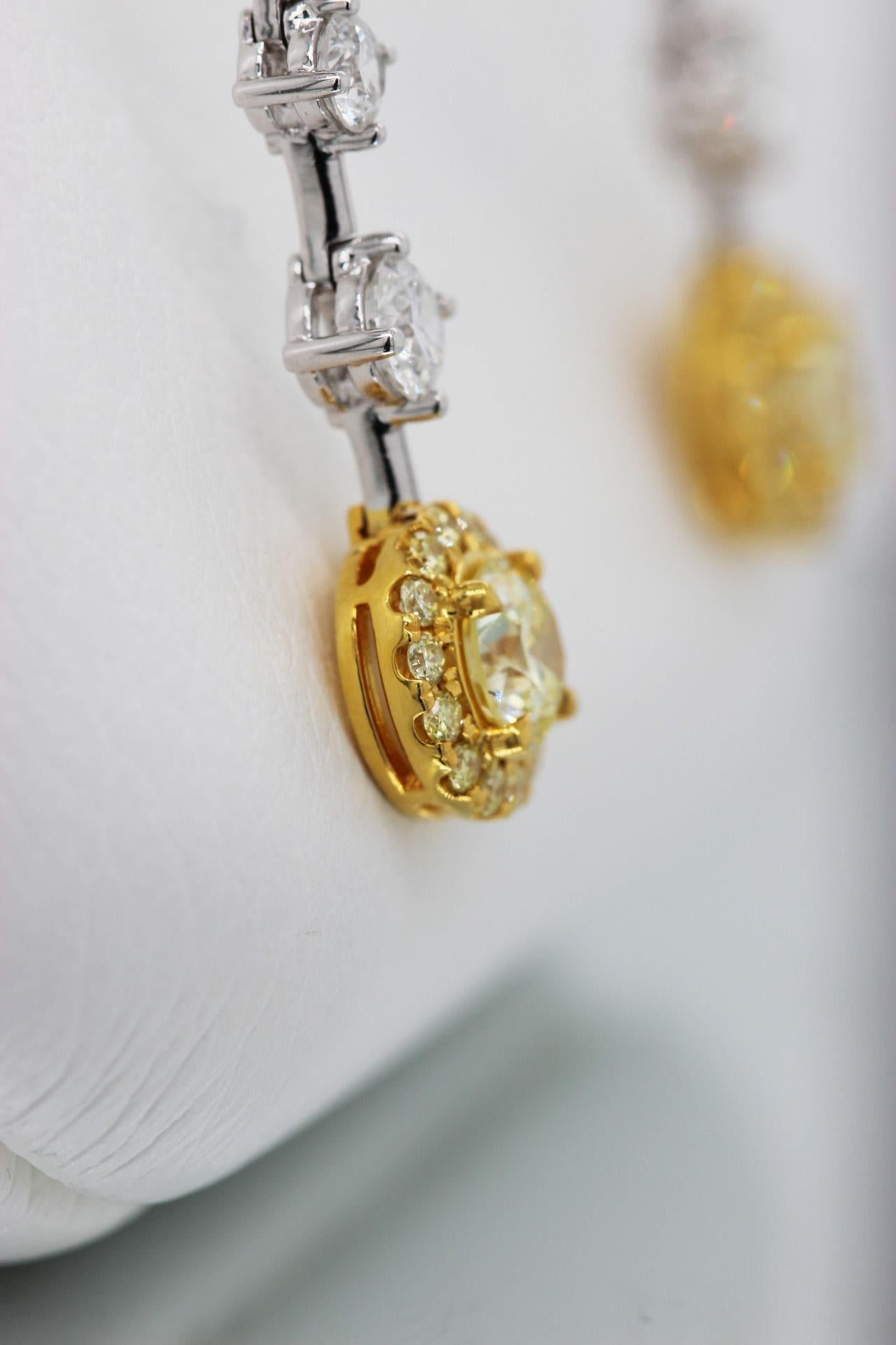A pair of graduated diamond dangle earrings with GIA-certified natural fancy yellow diamond center stones on 18k white gold. Dangle earrings made with white gold and graduated white round brilliant diamonds (F, 2.43 TCW) and round yellow diamond