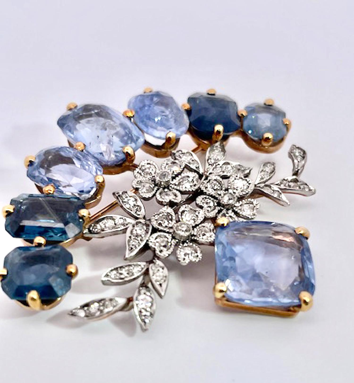 Questa spilla con diamanti e zaffiri a 18 carati è unica nel suo genere, poiché contiene oltre 20 carati di zaffiri.  Questi zaffiri sono di taglio ovale e di diversi colori, dall'azzurro chiaro, al blu medio e al blu scuro.  Sono incastonati in una