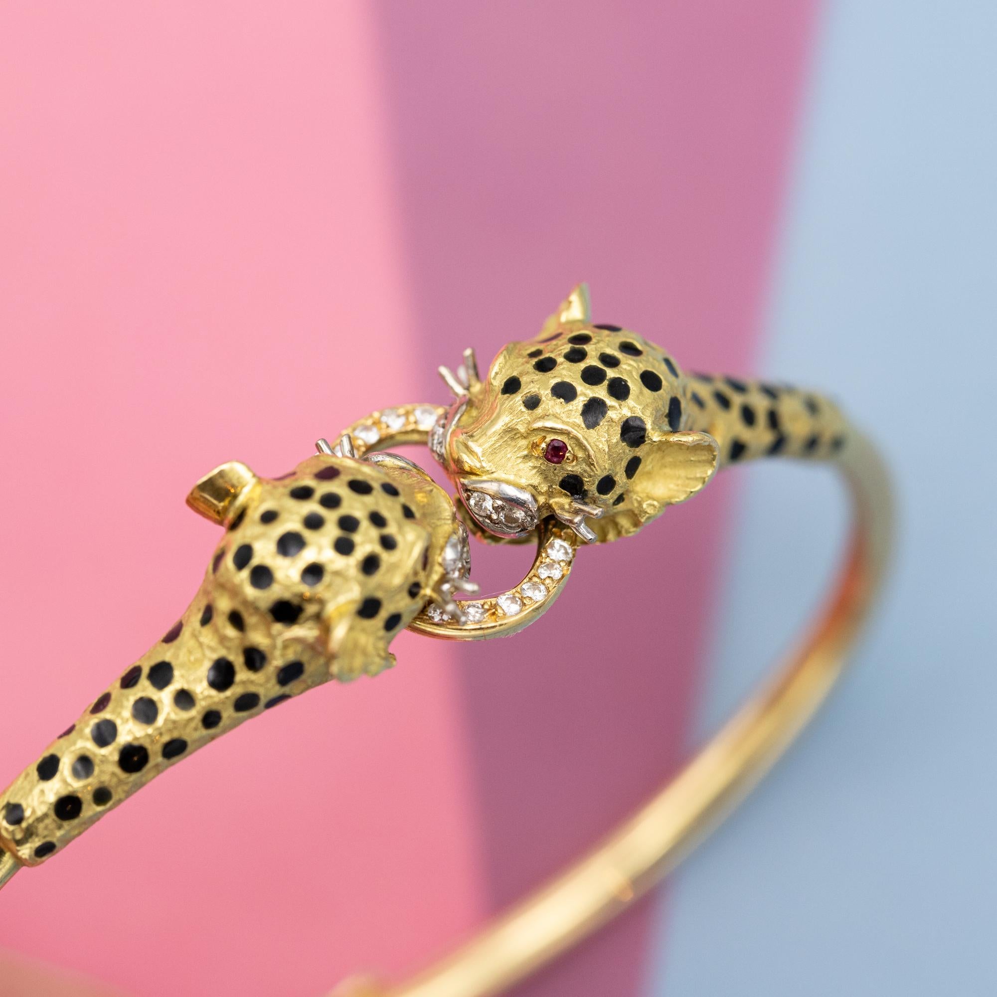 For sale is this wonderful 1980's bangle depicting two leopards biting the same diamond ring. This wonderful treasure is made in 18k yellow gold and decorated with black enamel spots. Both leopards have small ruby eyes, diamond set moustaches and