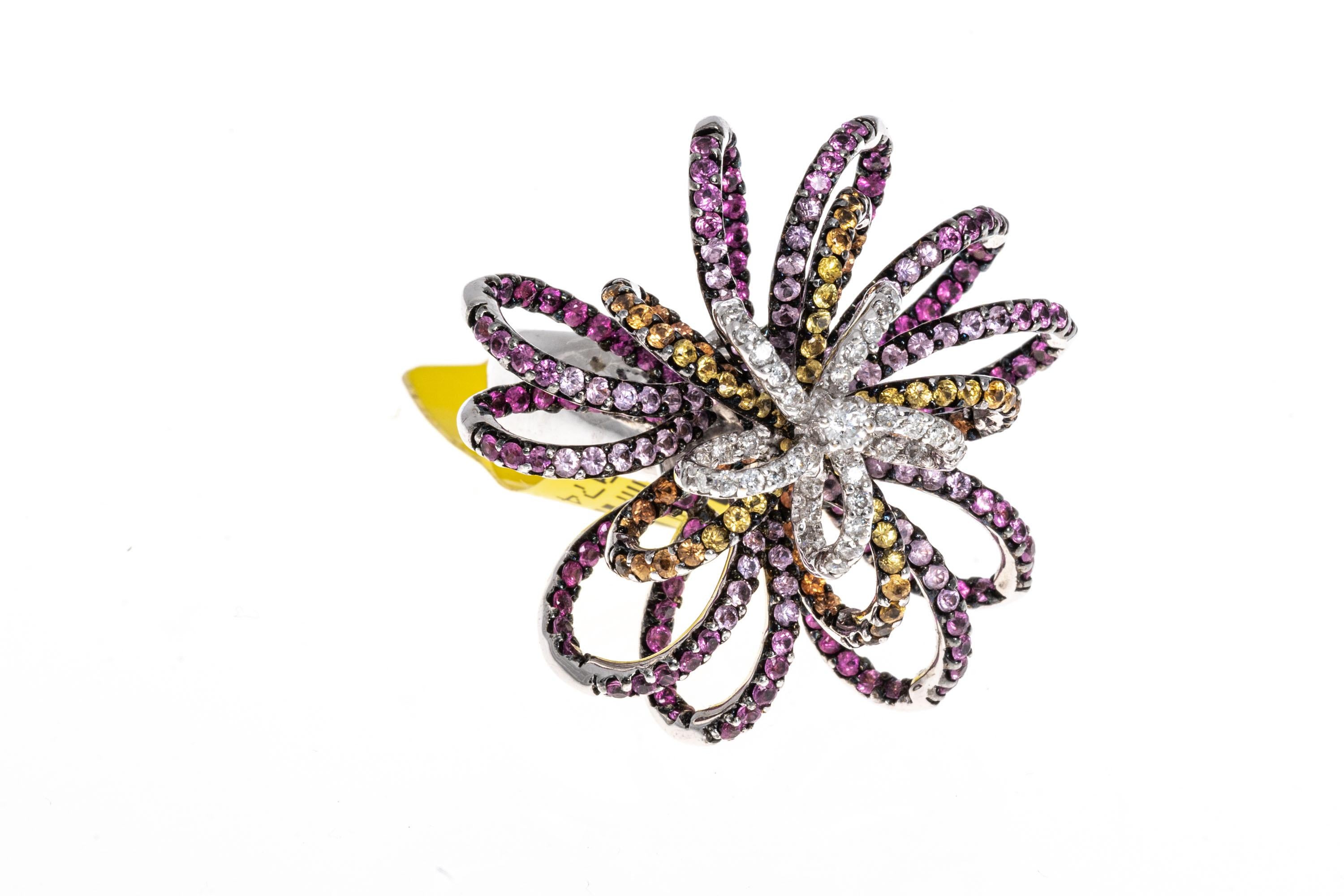 18k white gold ring. This amazing ring is a flower motif, consisting of open loops set with ombre dark to light pink round faceted sapphires, alternating with ombre dark to light yellow round faceted sapphires, all prong set. In the center are round
