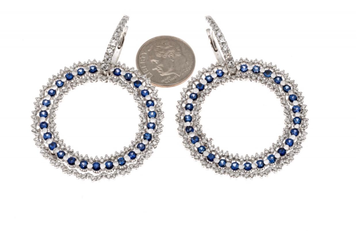 These beautiful, versatile earrings contain a hoop top, set with a graduated row of round brilliant cut white diamonds. Suspended from the hoop is a circle shaped open drop style pendant, bordered on both sides by round faceted, white diamonds,