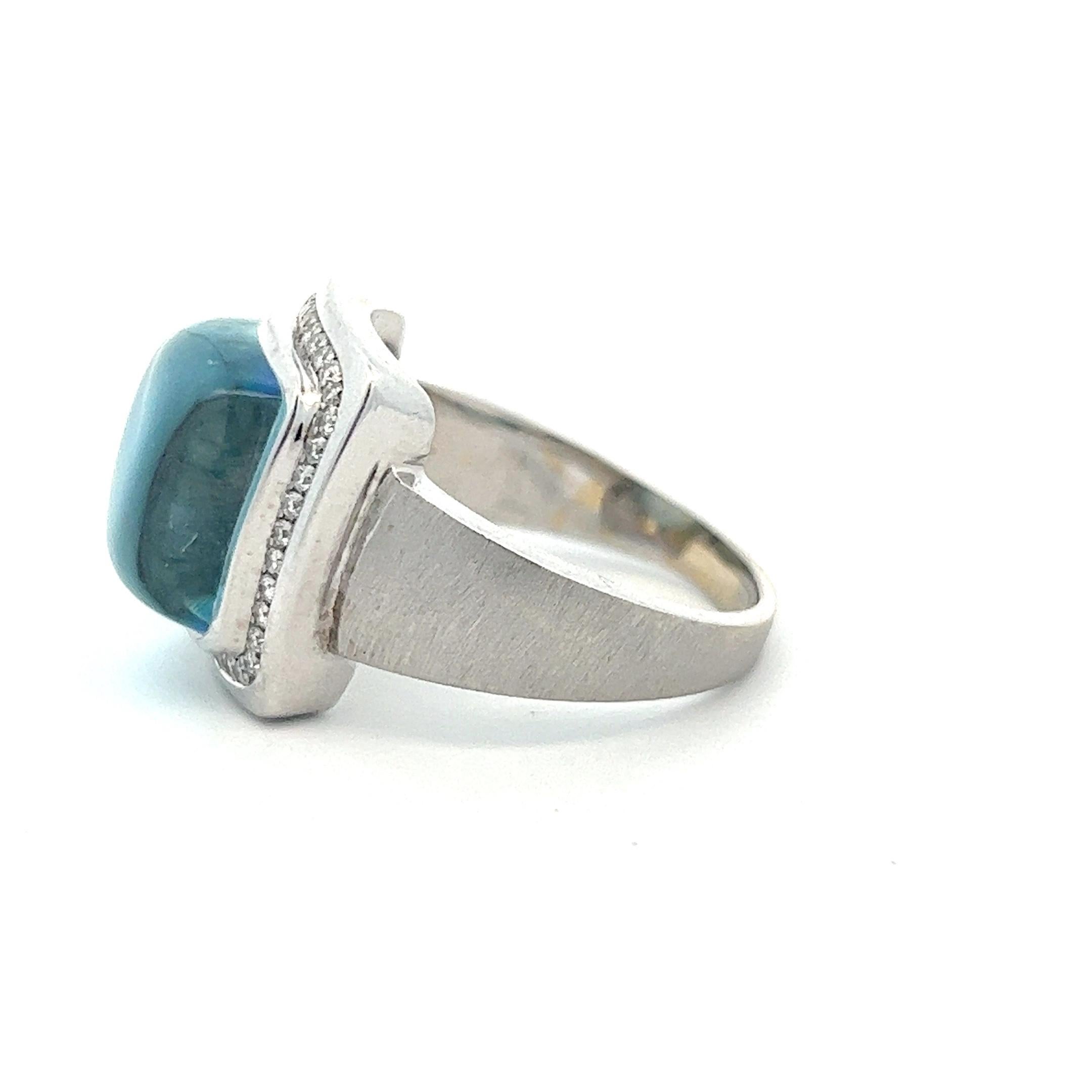 A beautiful cabochon blue topaz set within a halo of small small diamonds in an 18k white gold setting. The topaz is a peaceful sky blue and, measured in setting, weighs approximately 14.79 carats. The ring is crafted of 18k white gold with a