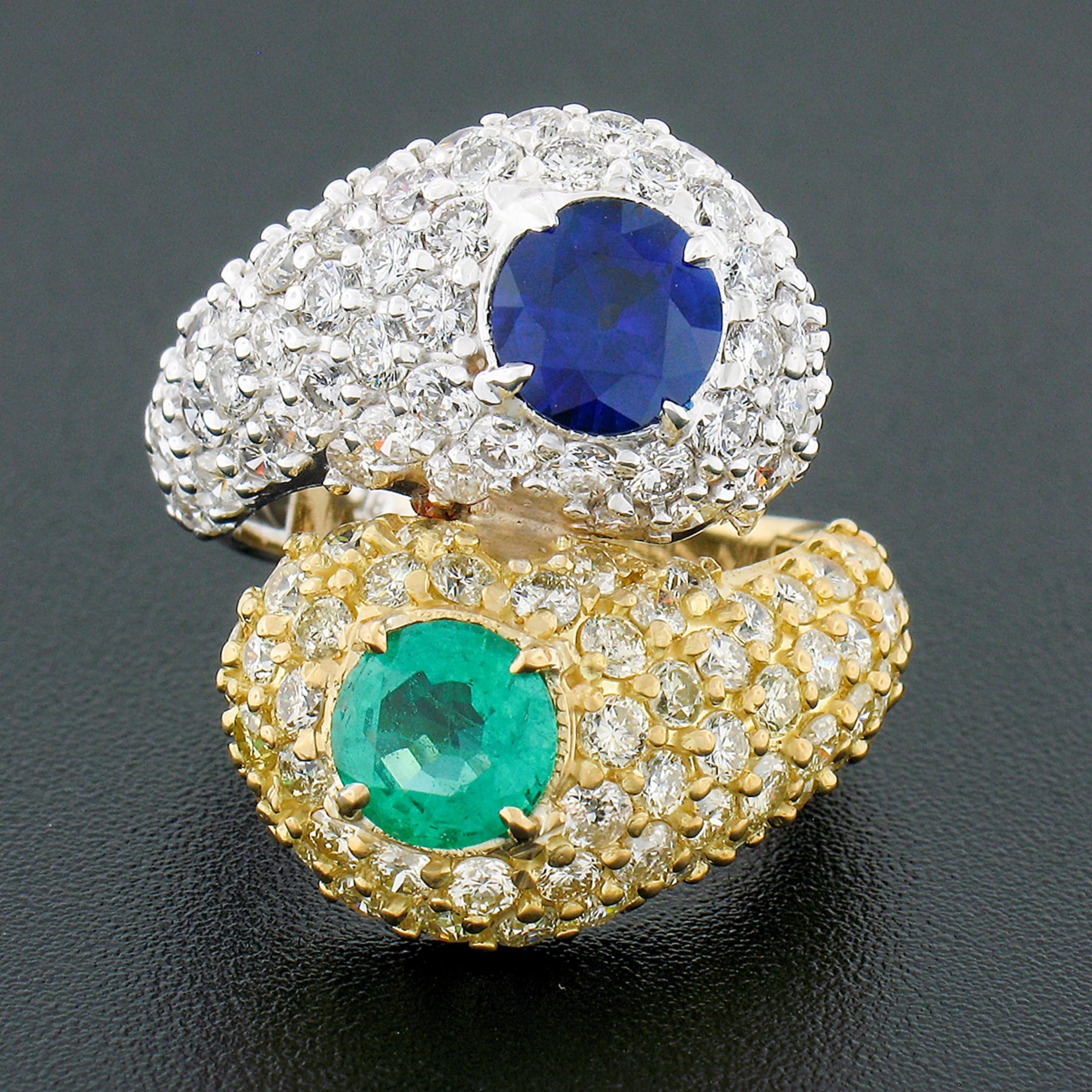 Here we have a truly stunning ring which is crafted in solid 18k yellow and white gold featuring an elegant bypass style that is neatly set with a round brilliant cut sapphire and emerald and drenched with diamonds throughout its top. The white gold