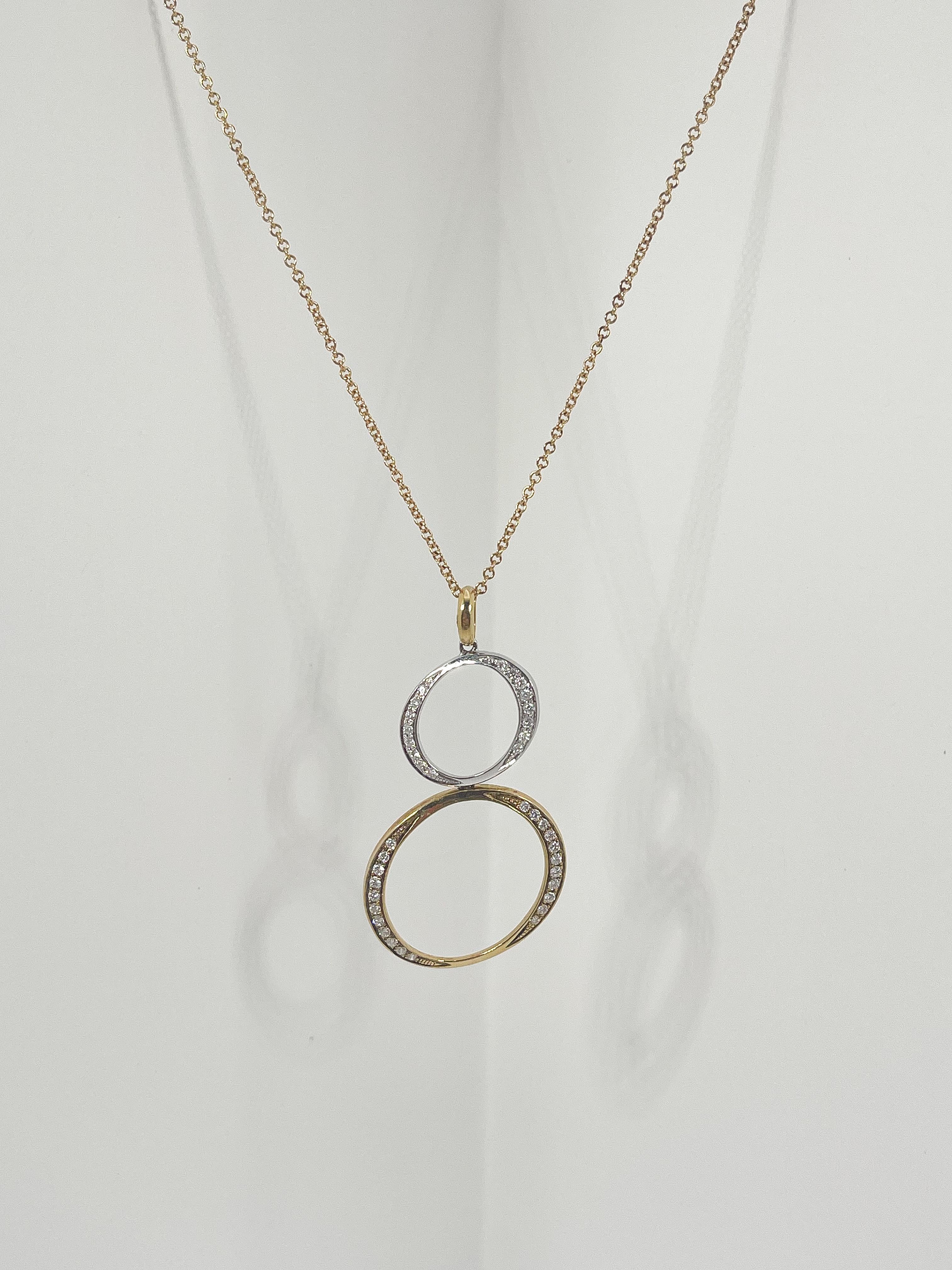 18k two toned diamond .30 CTW double circle pendant necklace. The chain and bail are both yellow gold, the top circle is white gold, and the bottom circle is yellow gold, both circles have diamonds on both sides of the circle. The necklace is 18