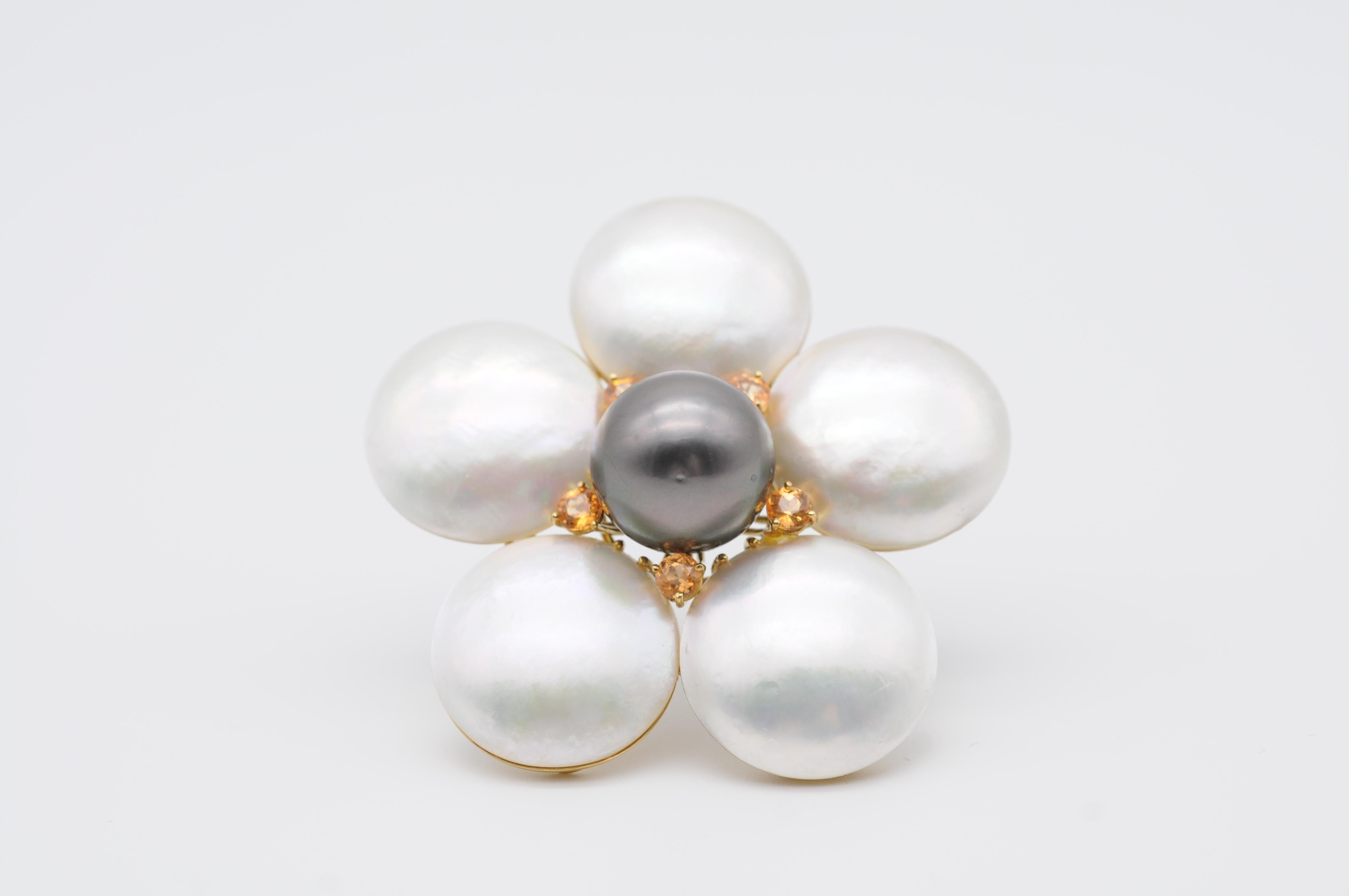This unique pearl brooch is a true masterpiece of craftsmanship and design. It features a large flower-shaped setting made of 18k solid yellow gold, which showcases a stunning black Tahitian pearl in the center. The lustrous pearl shimmers with