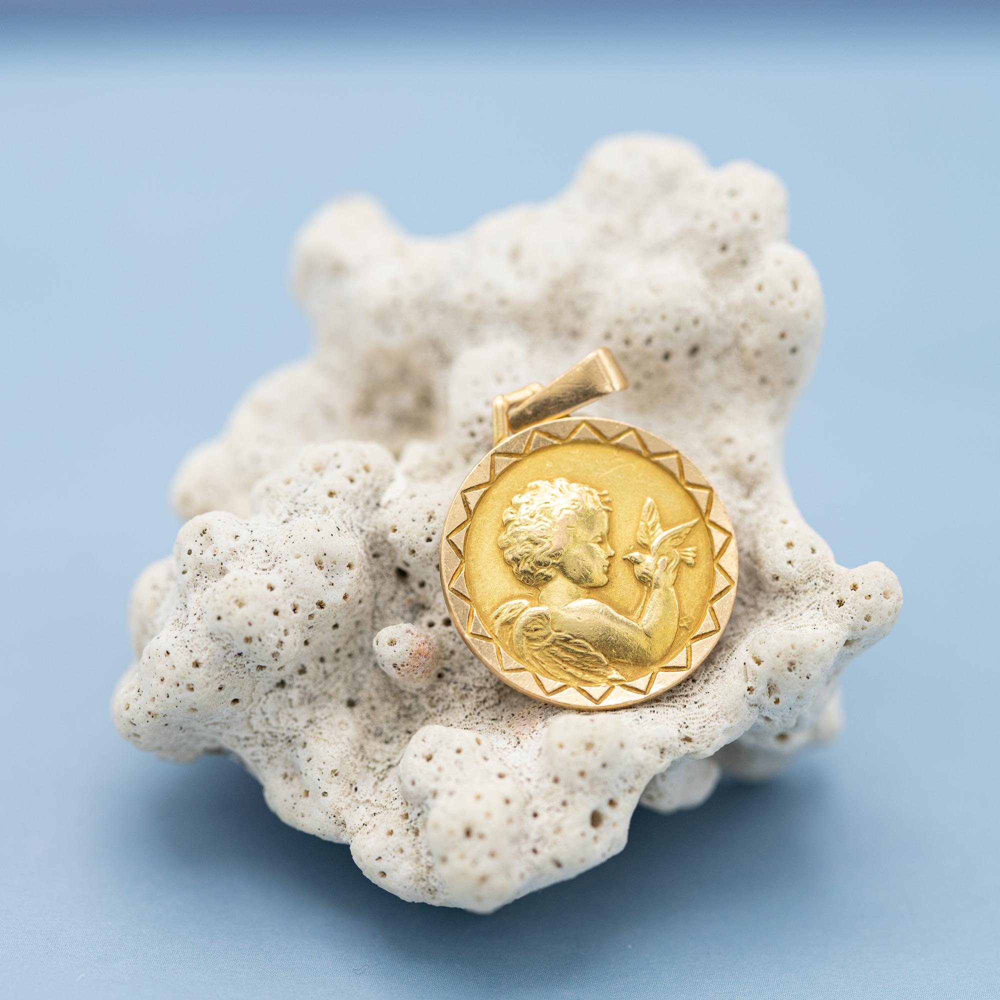 For sale is this 18 Karat solid yellow gold cherub pendant. This beautiful detailed medal depicts a little angel with wings holding a dove. Thanks to the many details of this little angel his curly hair and stunning wings are clearly visible. This