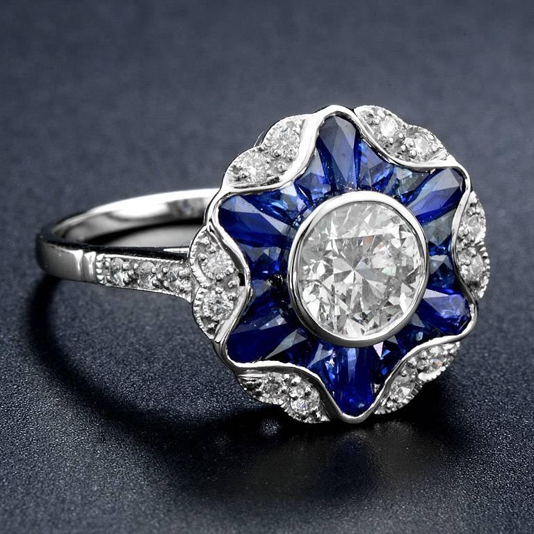 Brilliant Cut Diamond 1.05 Carat (SI Clarity) set on 18K White Gold Ring.  Flower cluster around the center by French Cut Thai Blue Sapphire Total 2.00 Carat channel set and small melee Diamond 0.25 Carat.

The ring was made in size US#7