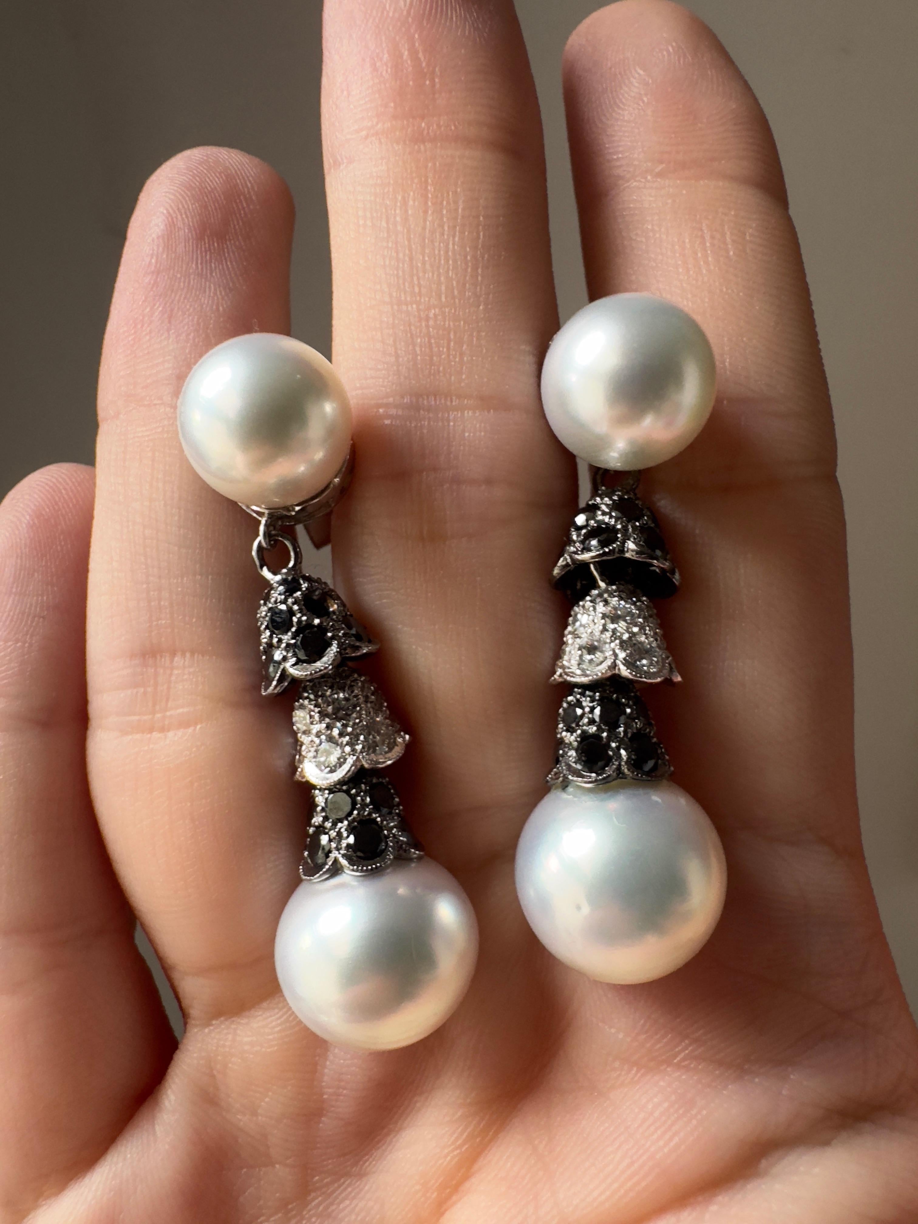 Questi orecchini a goccia con perle e diamanti in oro bianco 18 carati incarnano l'eleganza. Ogni orecchino inizia con una perla naturale di 10,96 mm, seguita da un trio a cascata di tappi smerlati scolpiti in movimento, con 6,11 carati di diamanti