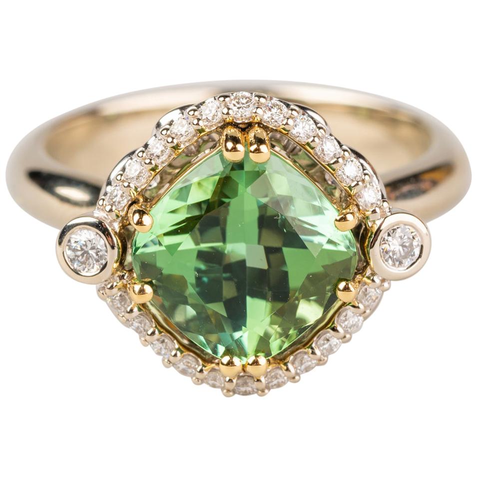 An 18k white and yellow gold ring set with one 2.81 carat cushion cut green tourmaline with a halo of twenty-two 1.2mm, and two 2mm white round F color VS clarity diamonds, 0.2 total carat weight. Ring size 7. This ring was made and designed by llyn
