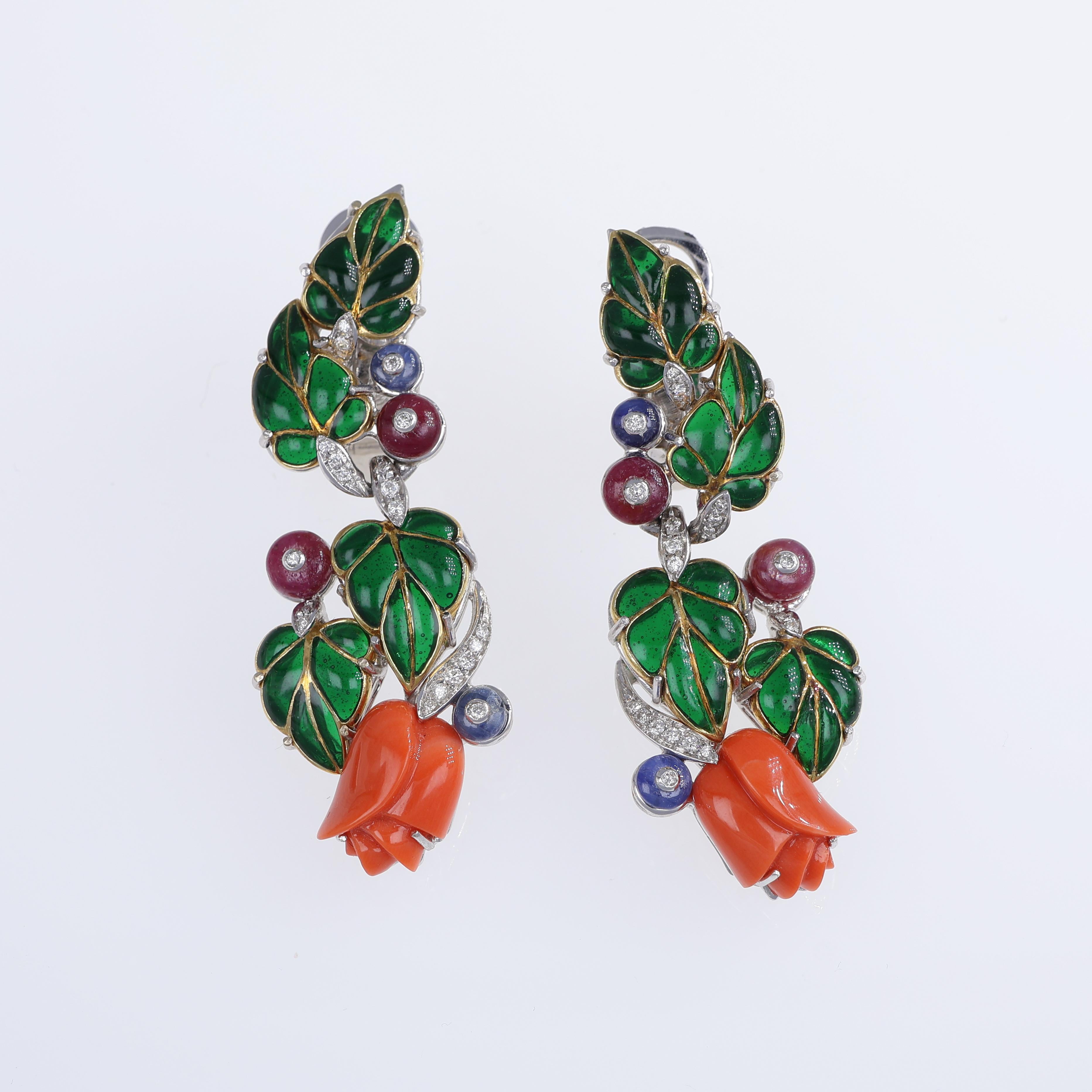 These exquisite 18K white and yellow gold drop earrings feature intricately carved natural coral flowers framed by a cascade of lush green enamel leaves. Adorned with cabochon-cut rubies, sapphires, and emeralds, each element is meticulously