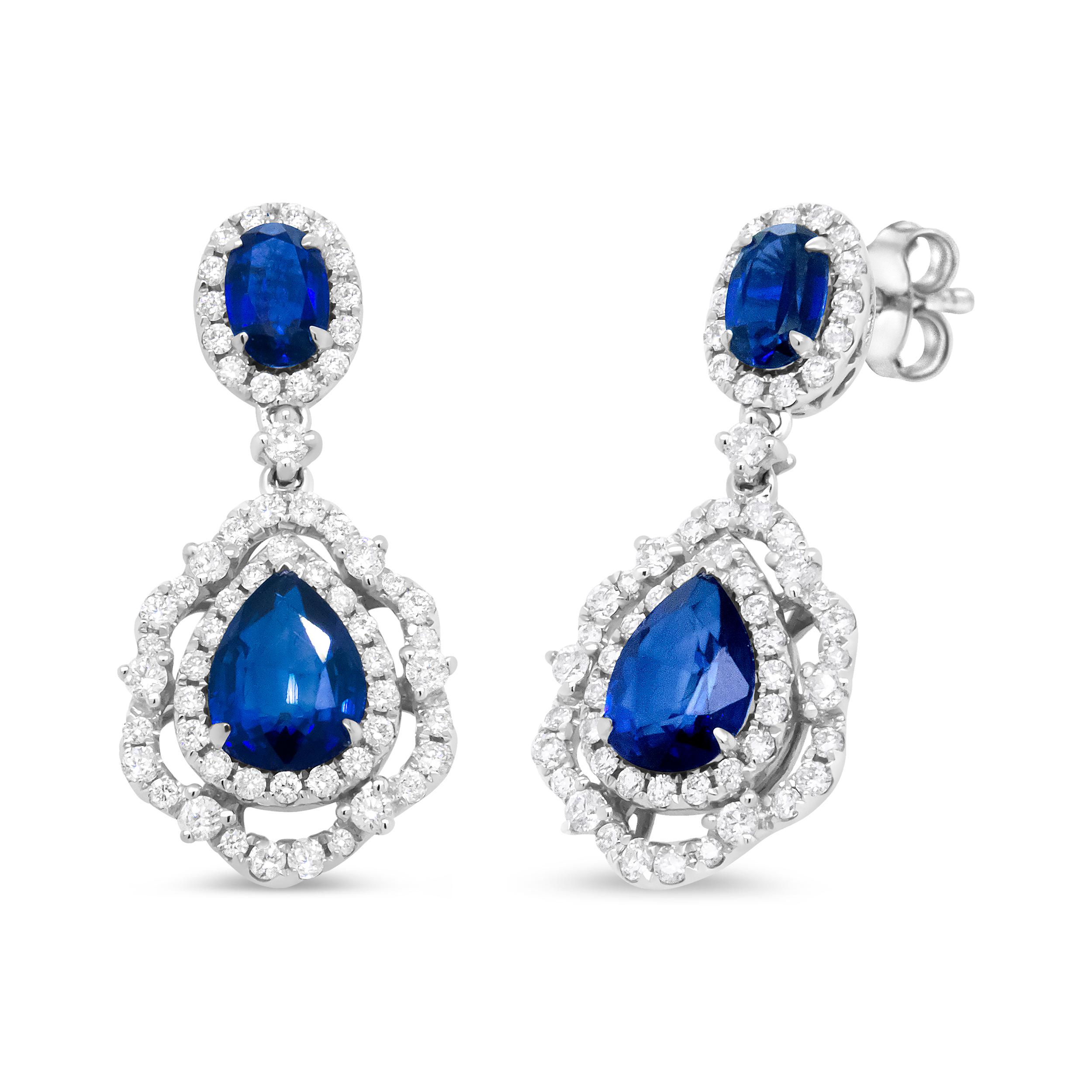 A stunner at every angle, this pair of dangle drop earrings is bathed in the sparkle of gemstones and diamonds. The upper dangle is centered by a magnificent  5.5 x 3.5 oval-cut tanzanite in a color-treated blue. A halo of glittering round diamonds