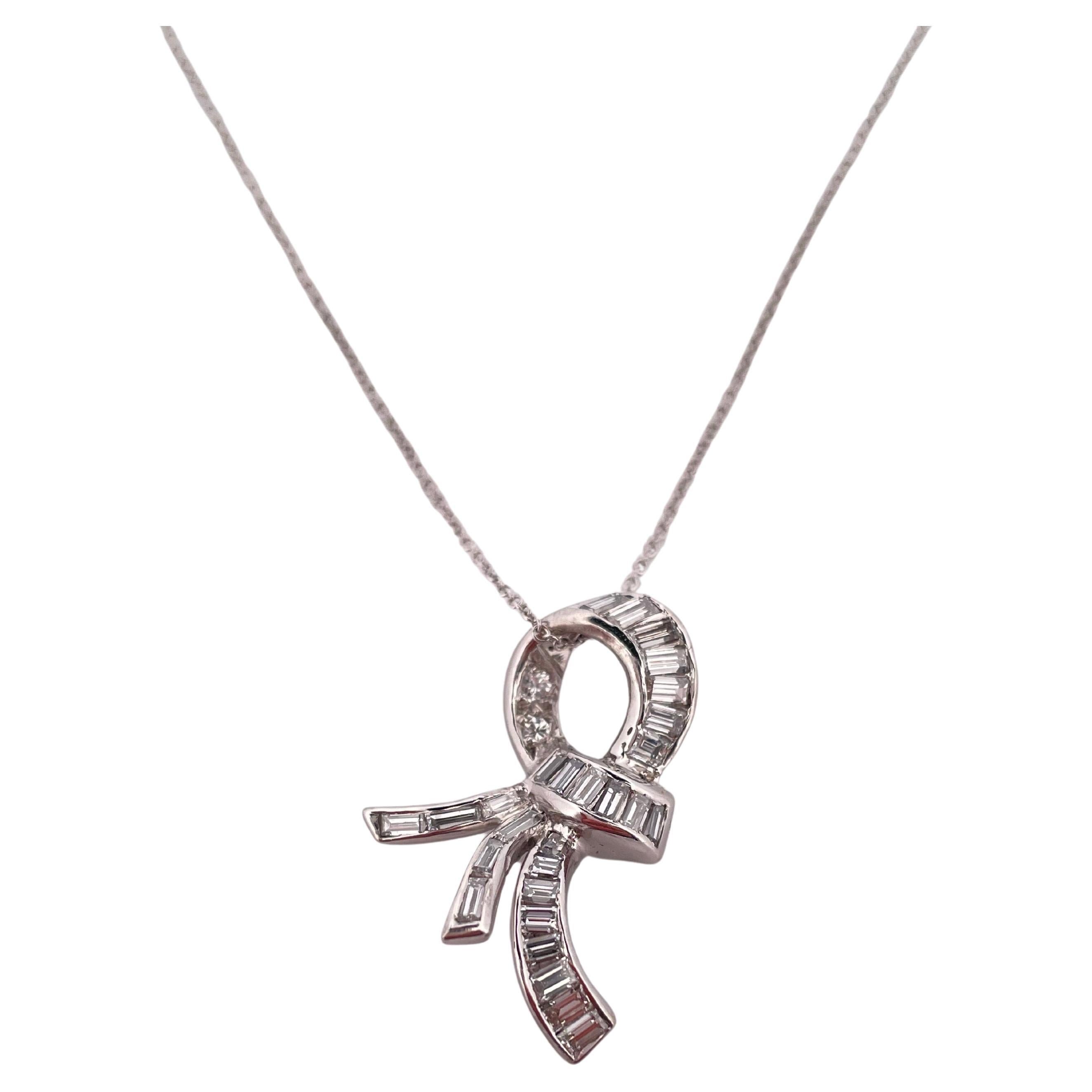 Questo elegante ciondolo e catena in oro bianco 18 carati emana una raffinatezza senza tempo grazie al suo grazioso design ispirato al nastro. Il pendente sfoggia 1,10 carati di peso totale di diamanti abbaglianti, tra cui tagli brillanti a baguette